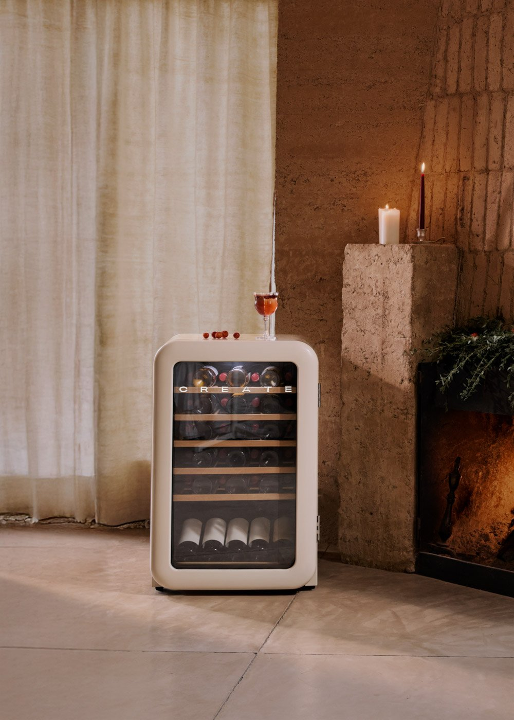 Una nevera de vino crema junto a una pared. Una bebida con bayas encima. Una chimenea con velas a la derecha.