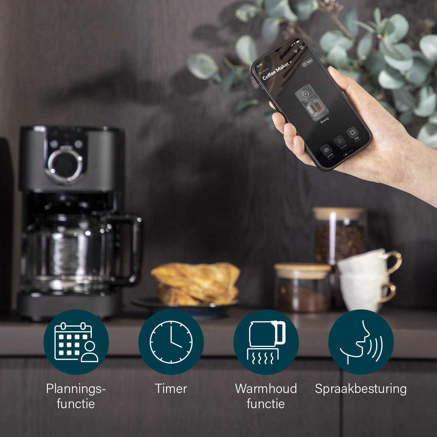 Dłoń trzyma telefon z aplikacją do ekspresu do kawy. Widoczny jest ekspres do kawy. Obecne są ikony timera i sterowania głosowego.