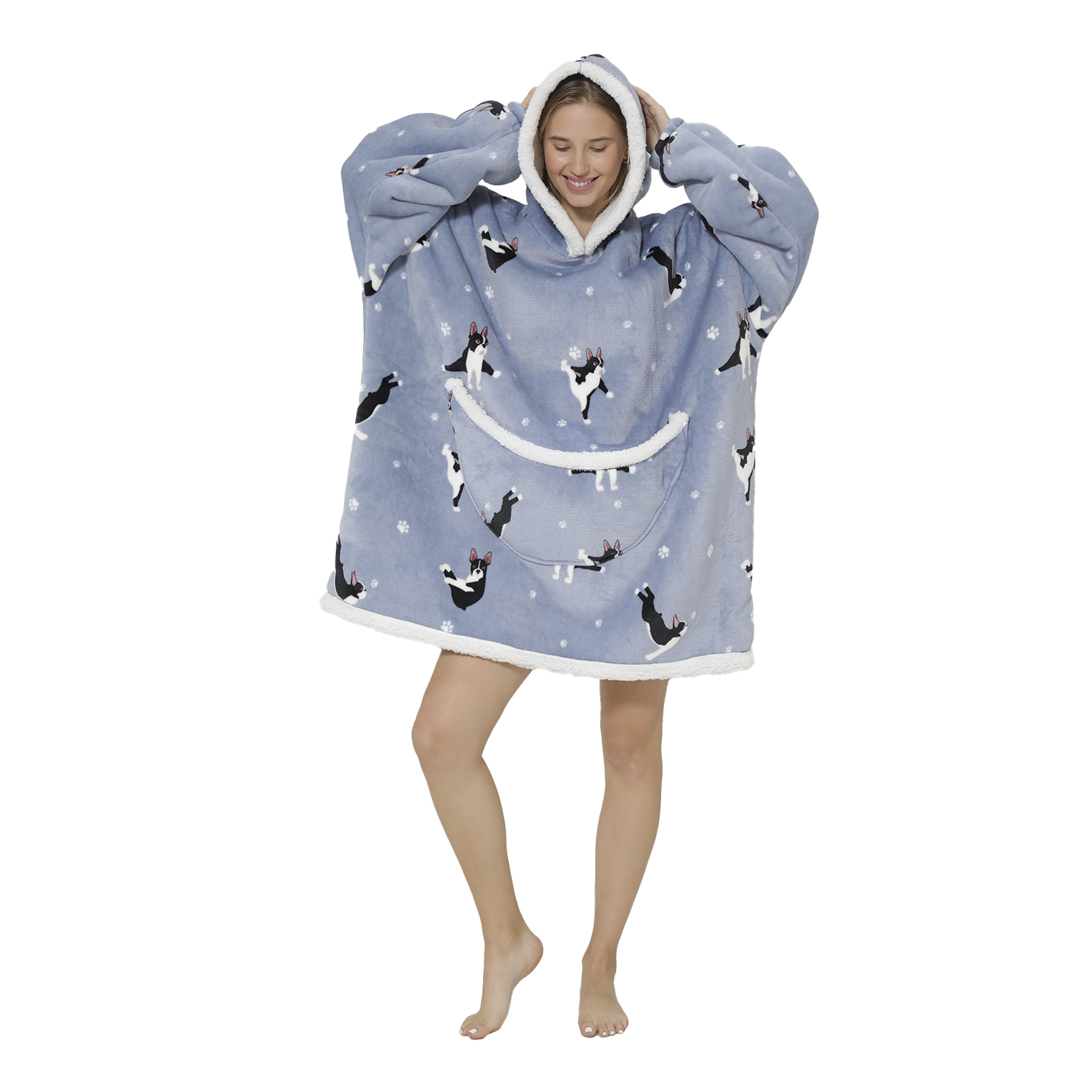 Una mujer con una sudadera azul con estampado de gato, ribete blanco y un bolsillo. Sonríe y se agarra la cabeza. Piernas desnudas, fondo blanco.