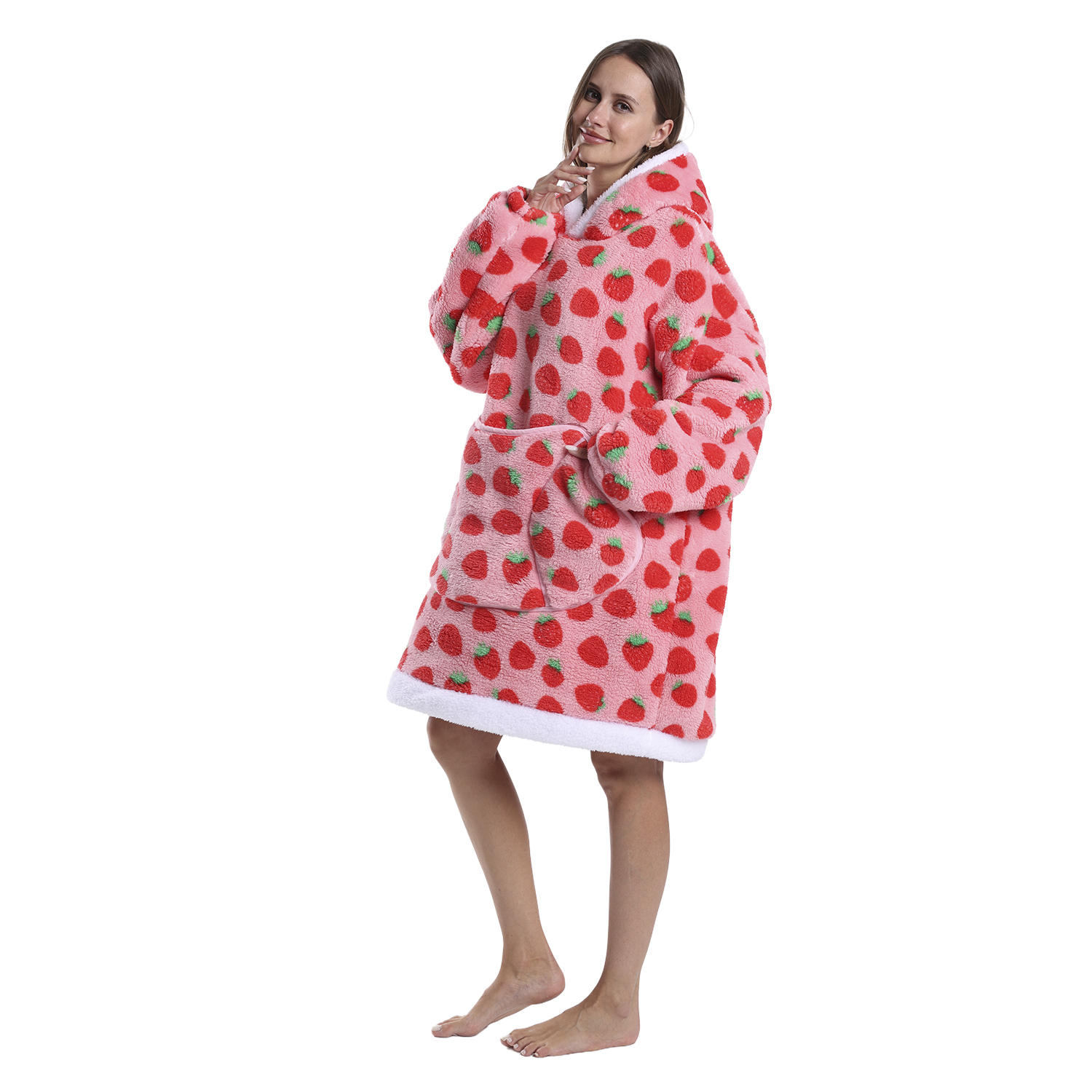 Una donna è in piedi con una felpa con cappuccio rosa a stampa fragole. Sorride, tenendosi il mento. Sfondo bianco. Piedi nudi.
