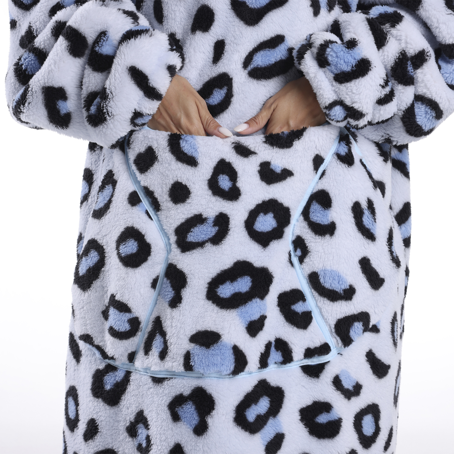 Una persona indossa una coperta leopardata blu chiaro e nera con le mani in tasca. Lo sfondo è bianco.