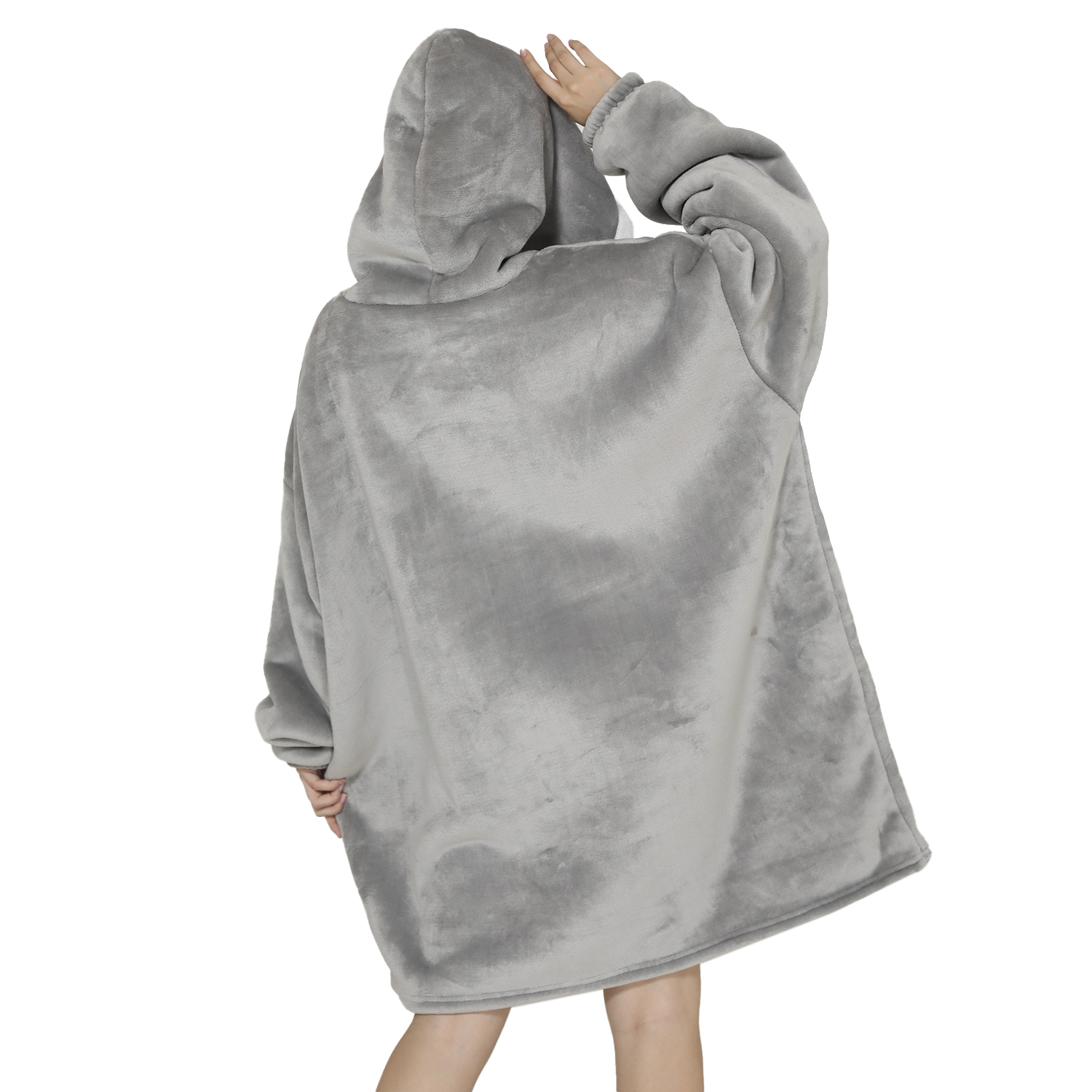 Una persona con una sudadera con capucha grande y gris con la capucha puesta, con los brazos levantados. El fondo es blanco.
