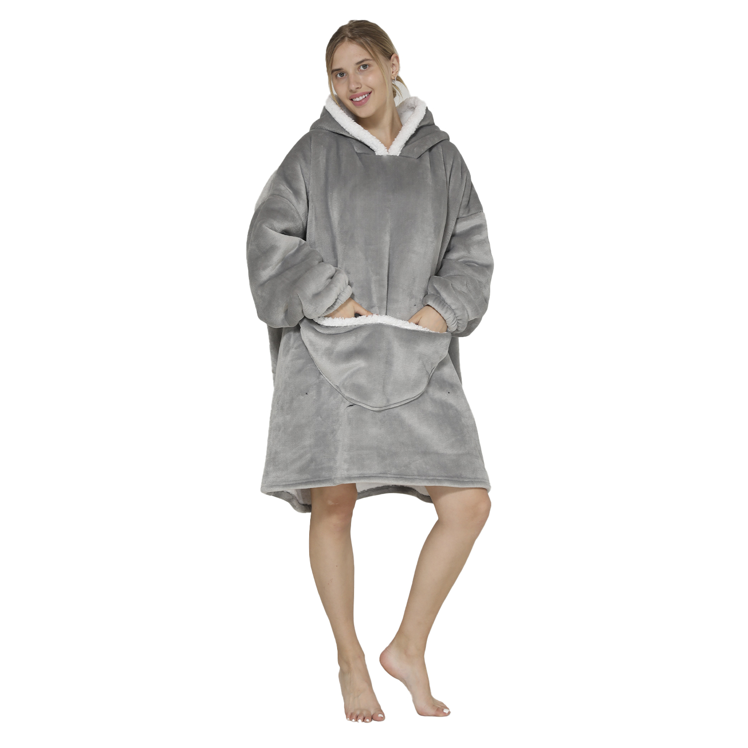 Una mujer con una sudadera gris con capucha sonríe. Está de pie sobre un fondo blanco, descalza. La sudadera tiene un forro blanco y esponjoso.