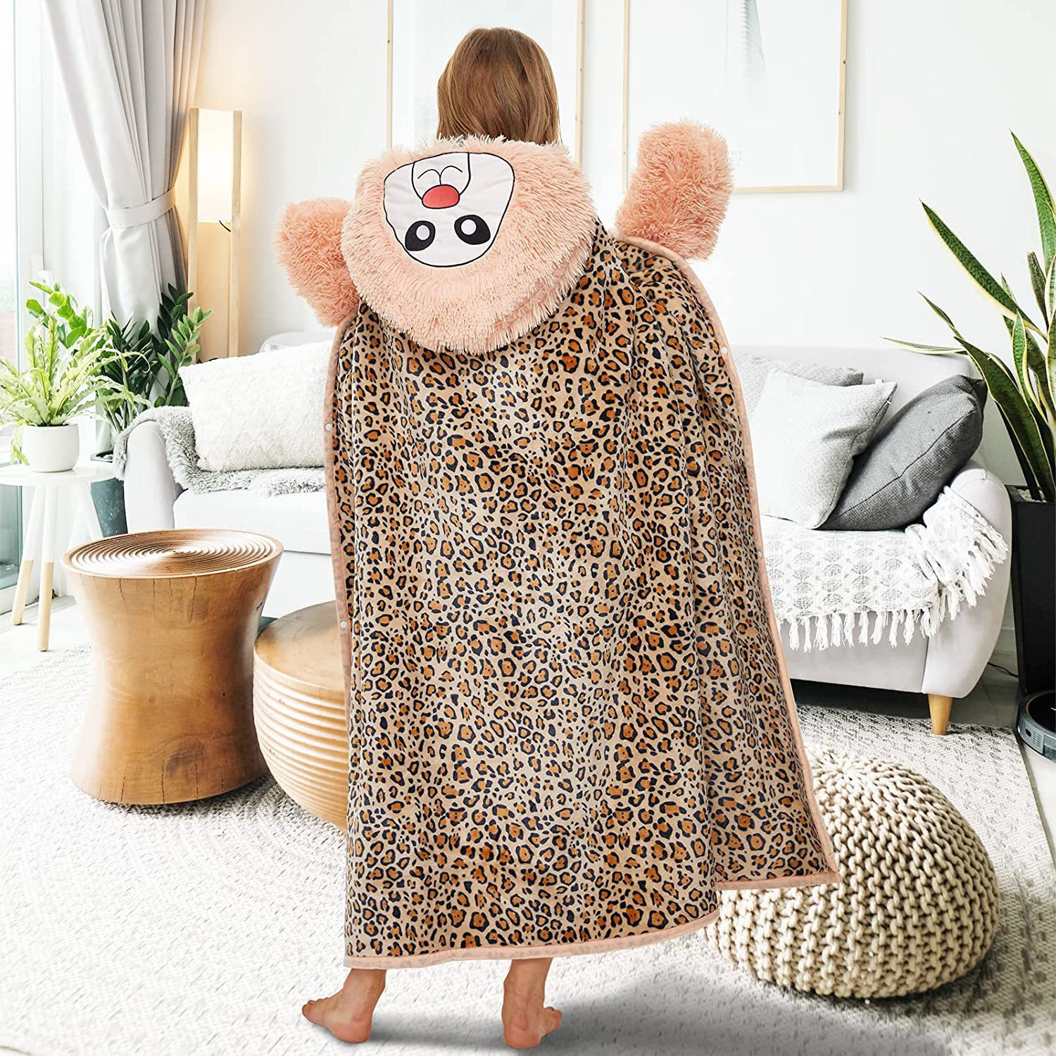 Una persona indossa una coperta con stampa leopardata con cappuccio a forma di leone in un soggiorno. Sono visibili un divano e altri mobili.