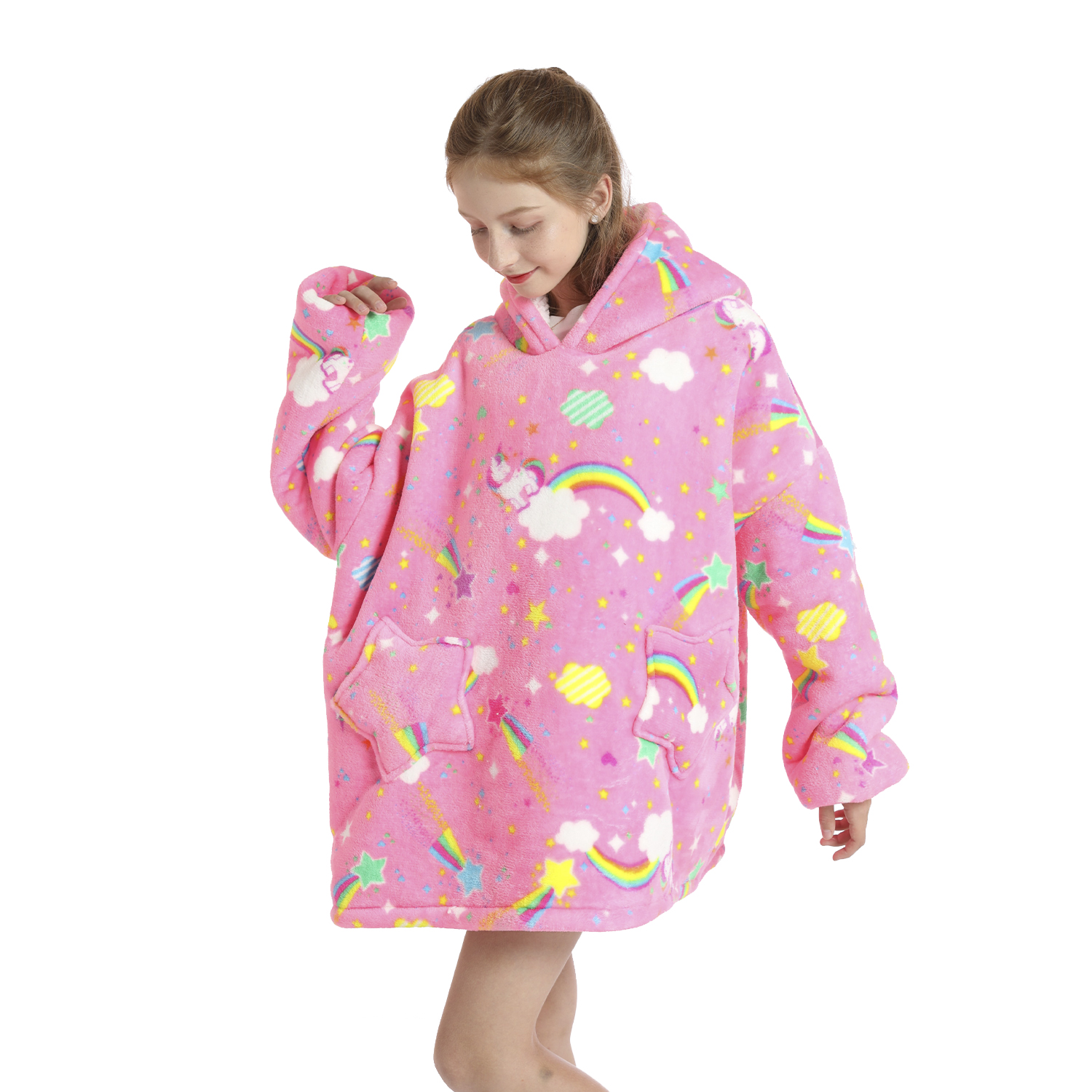 Una niña con una manta con capucha de unicornio rosa con arcoíris, estrellas y nubes. Mira hacia abajo y tiene el brazo levantado.