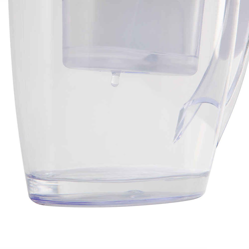 Una jarra de filtro de agua transparente con agua dentro. Una gota de agua cae del filtro. La jarra tiene un asa.