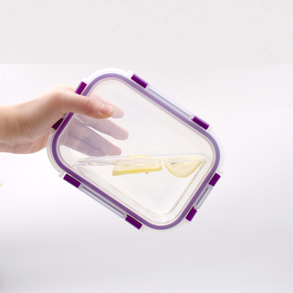 Una mano sostiene un recipiente rectangular transparente con detalles morados. Dentro, agua y rodajas de limón sobre un fondo blanco.