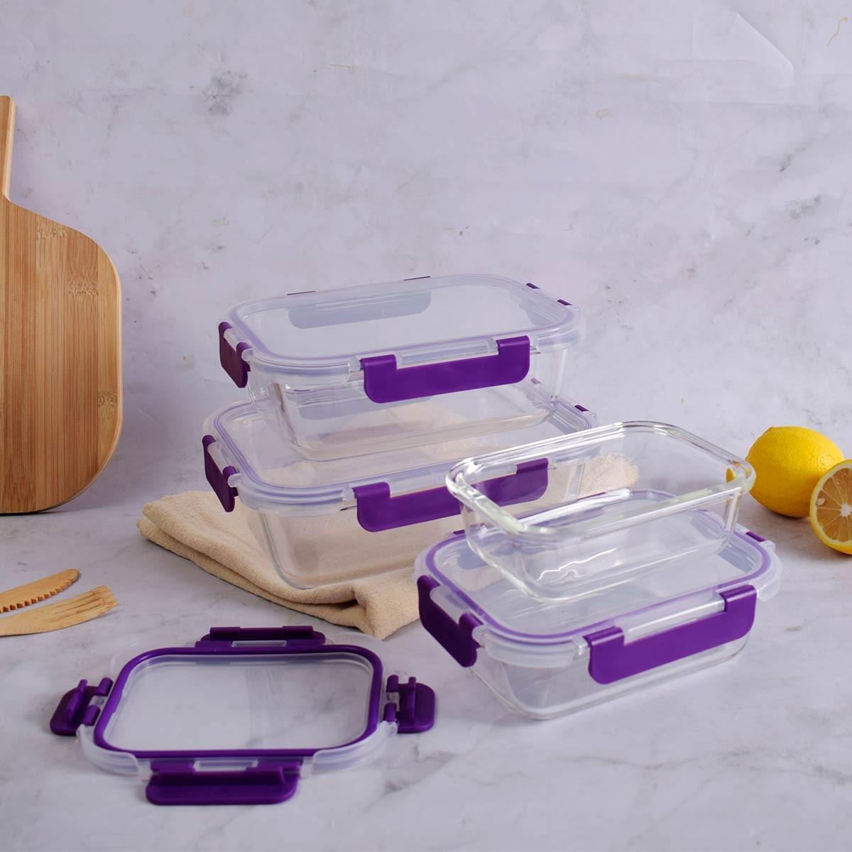 Varios recipientes de vidrio transparente con clips morados están dispuestos sobre una superficie de mármol. Un limón está cortado. Una tabla de madera está al lado.