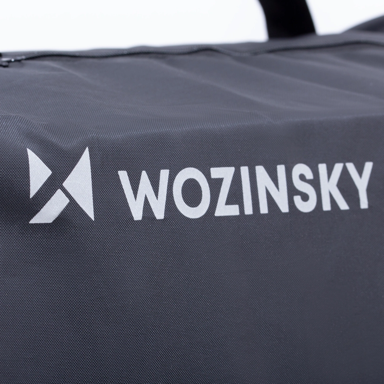 Nahaufnahme einer dunkelgrauen Tasche mit weißem WOZINSKY-Logo. Das Logo enthält einen stilisierten Pfeil. Der Hintergrund ist weiß.