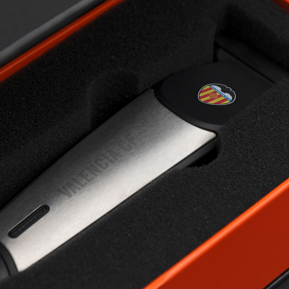 Un dispositivo metálico con 'VALENCIA CF' grabado. Descansa en una caja naranja forrada de espuma negra. Un logotipo es visible.