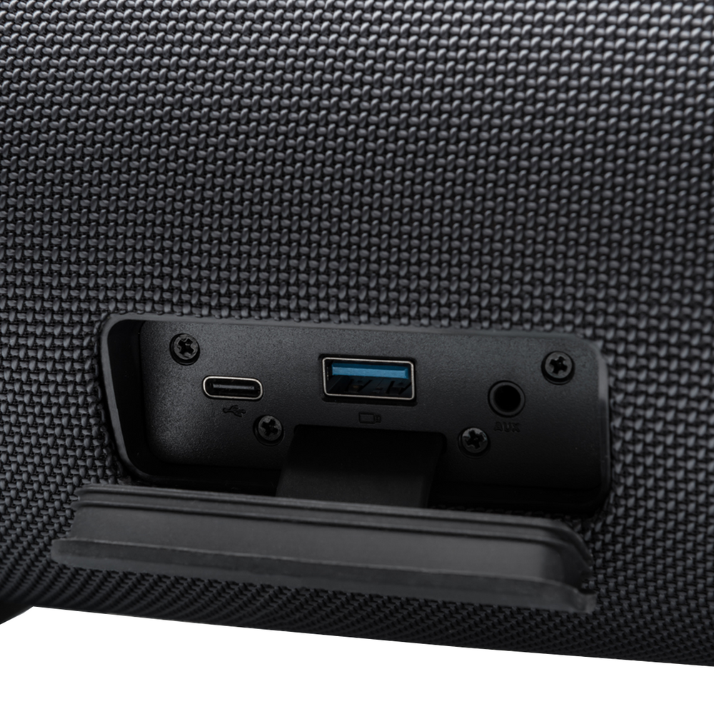 Zbliżenie czarnego głośnika z portami: USB, AUX i USB-C. Otwarta osłona. Głośnik ma teksturowaną powierzchnię.