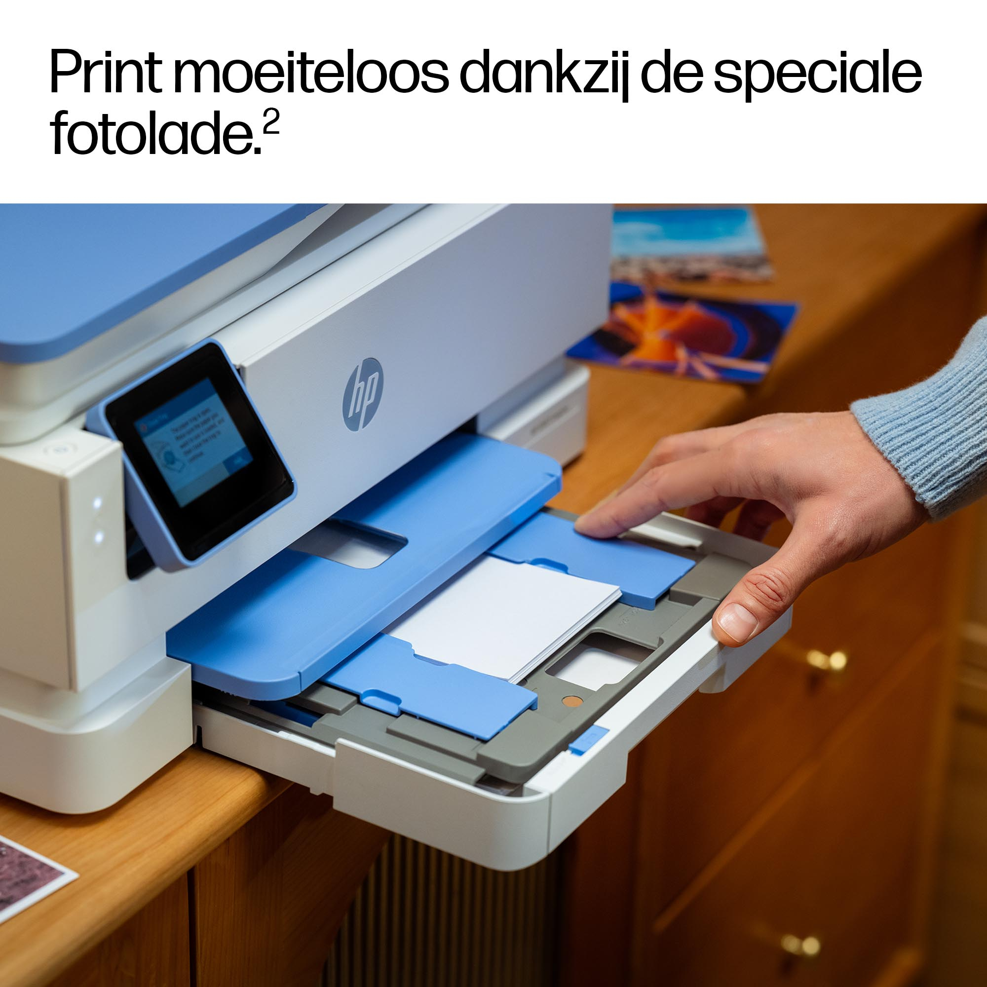 Ręka wyciąga tacę na papier z drukarki. Drukarka jest jasnoniebieska i biała. W tle zdjęcia.