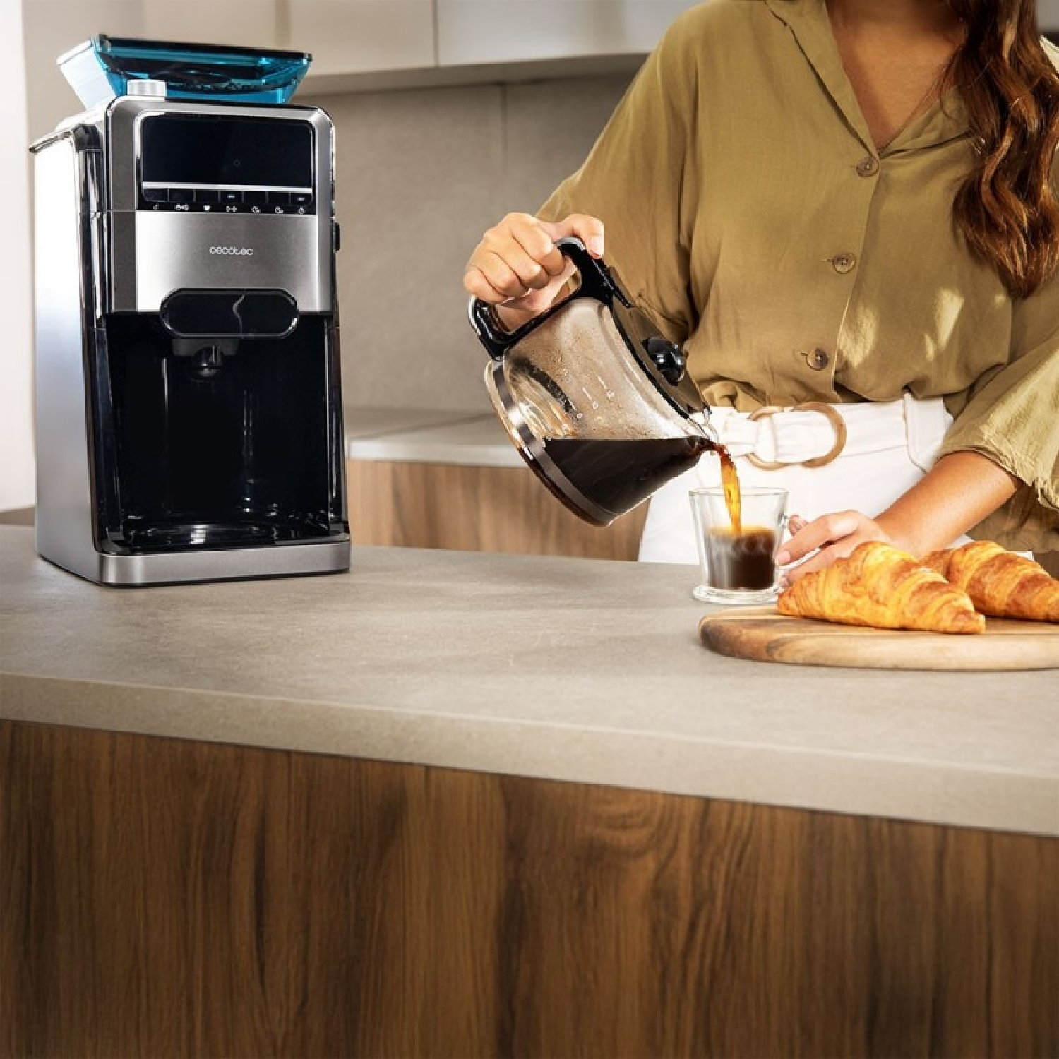 Una donna versa il caffè da una caraffa in un bicchiere. Macchina del caffè a sinistra. Croissant su un tagliere.