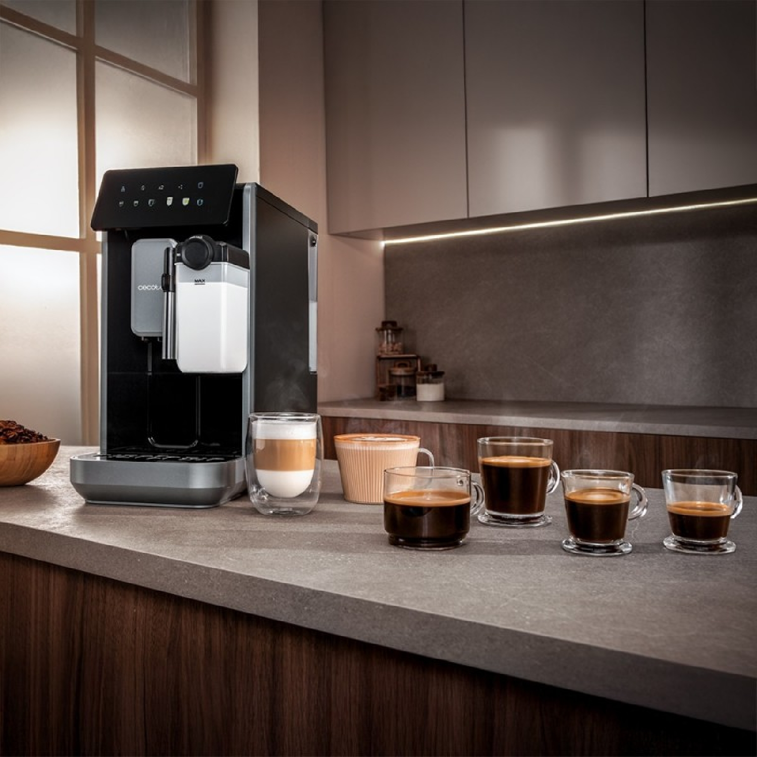 Una macchina da caffè con diverse tazze di caffè. Un bicchiere di latte macchiato e una ciotola di legno con chicchi di caffè sono sul bancone.