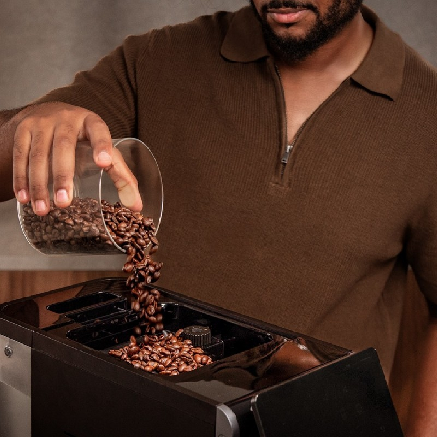 Un uomo versa chicchi di caffè da un bicchiere in una macchina da caffè nera. Indossa una camicia marrone. I fagioli cadono.