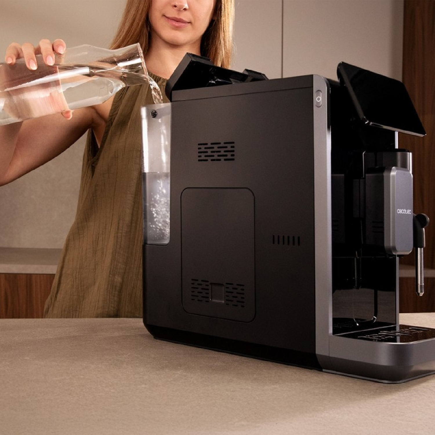 Una donna versa acqua in una macchina da caffè nera. La macchina è su un bancone. La donna indossa un top verde.