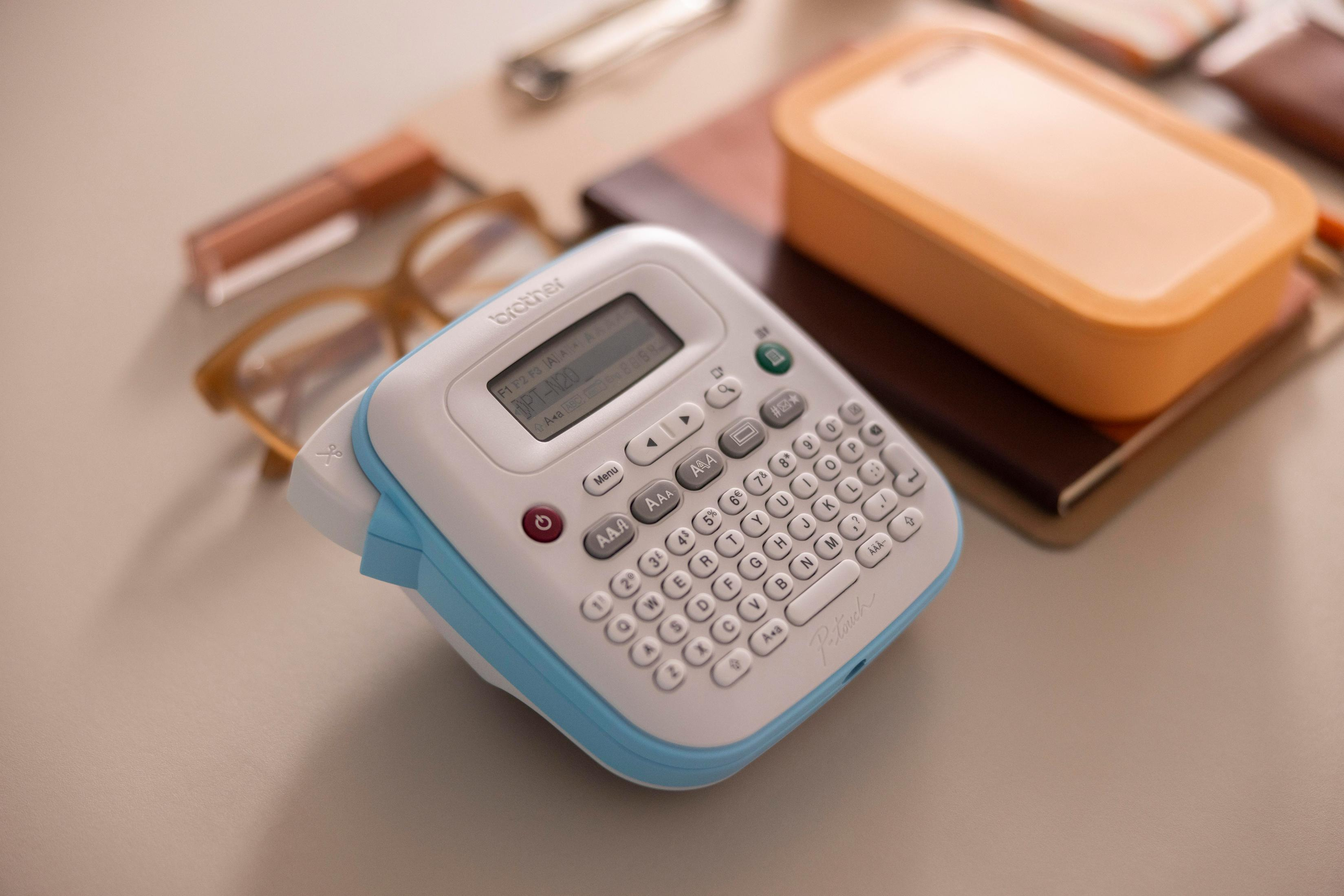 Etykieciarka z klawiaturą, ekranem i przyciskiem zasilania. Jest pudełko i okulary.