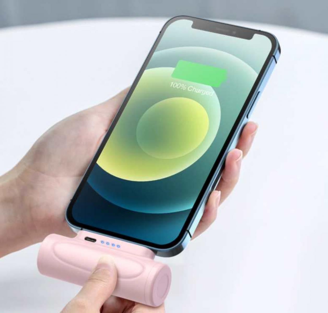 Eine Hand hält ein Smartphone, das mit einer pinkfarbenen Powerbank geladen wird. Das Telefon zeigt 100 % geladen an. Weißer Hintergrund.