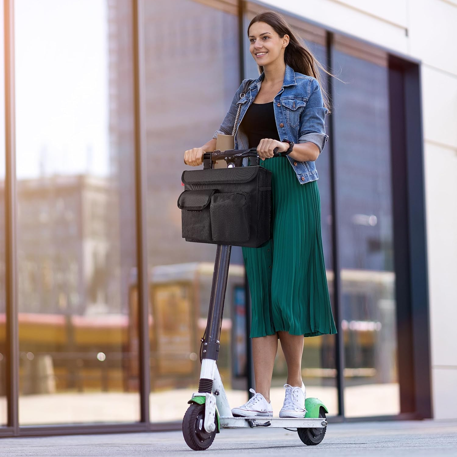 Eine Frau fährt mit einem E-Scooter, trägt eine Jeansjacke und einen grünen Rock. Auf dem Roller befindet sich eine schwarze Tasche.