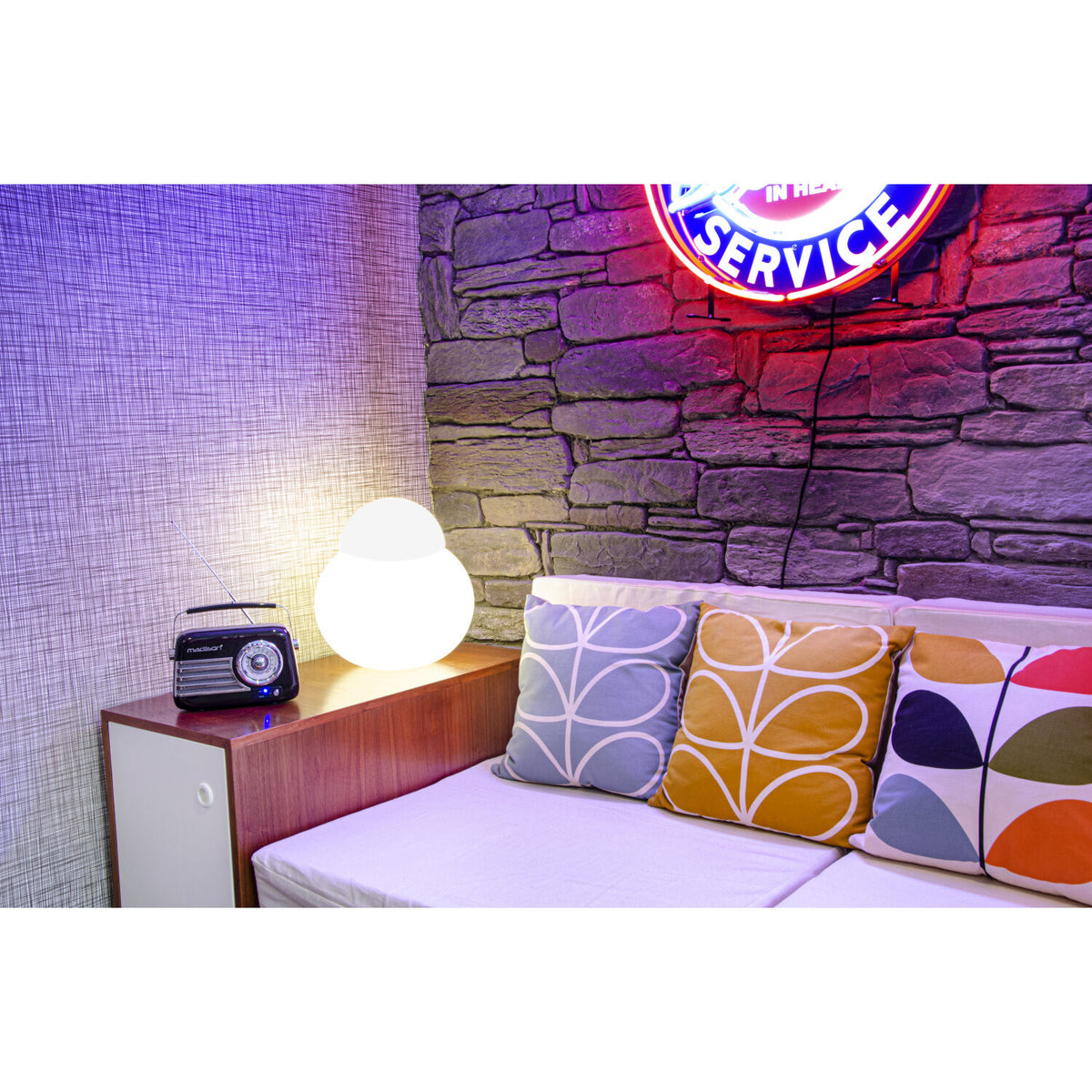 Ein Raum mit einem Sofa mit Kissen, einer Lampe, einem Radio und einem Leuchtschild mit der Aufschrift Service.