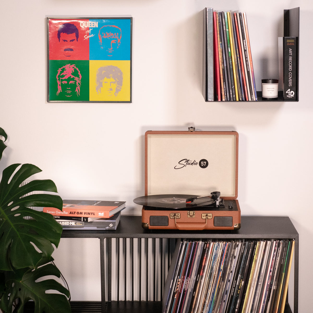 Queen-Albumcover an der Wand. Plattenspieler auf einem Regal. Vinylplatten sind unten gelagert. Links eine Pflanze.