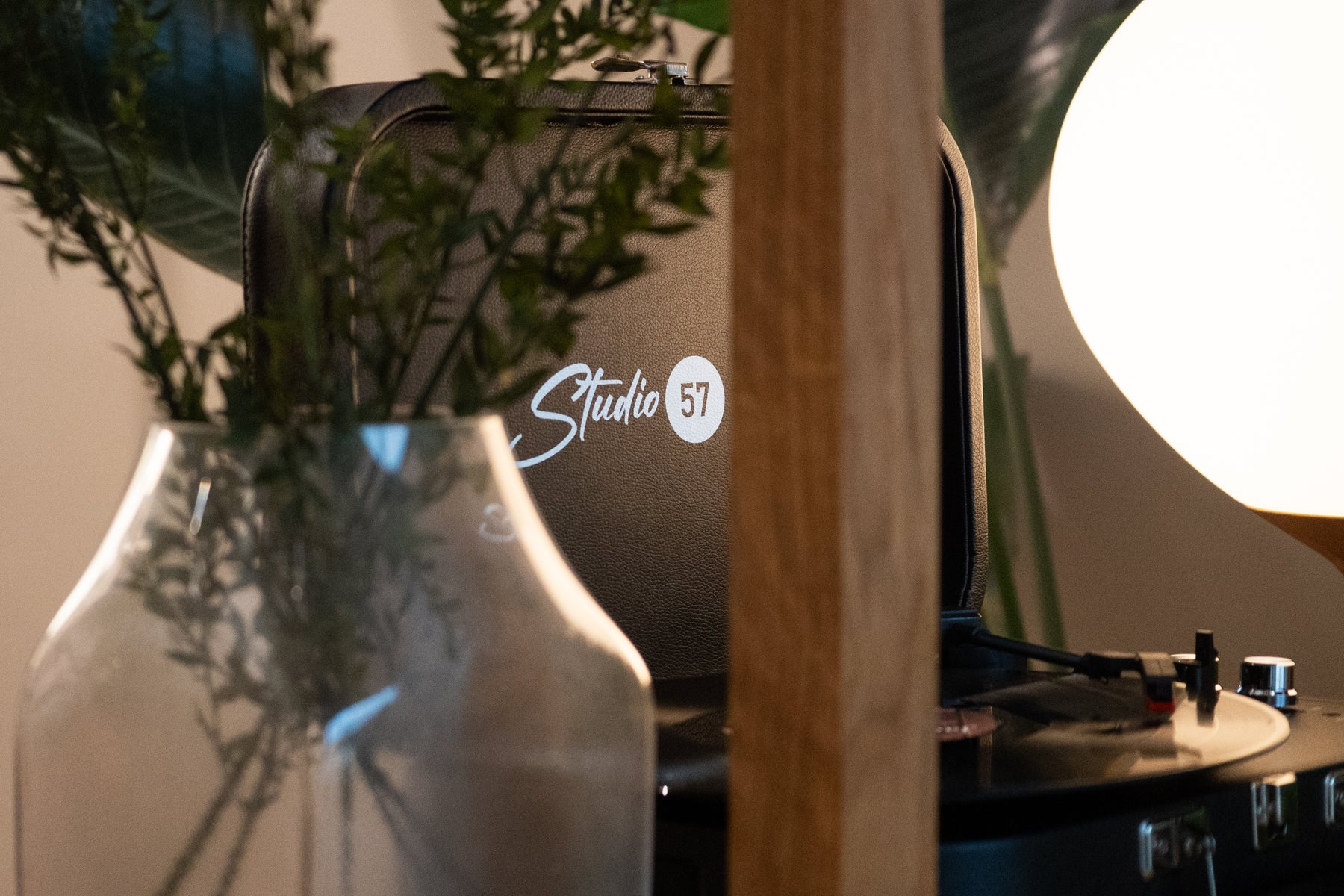 Ein Plattenspieler mit 'Studio 57', eine Vase mit Pflanzen und eine leuchtende Lampe sind zu sehen.