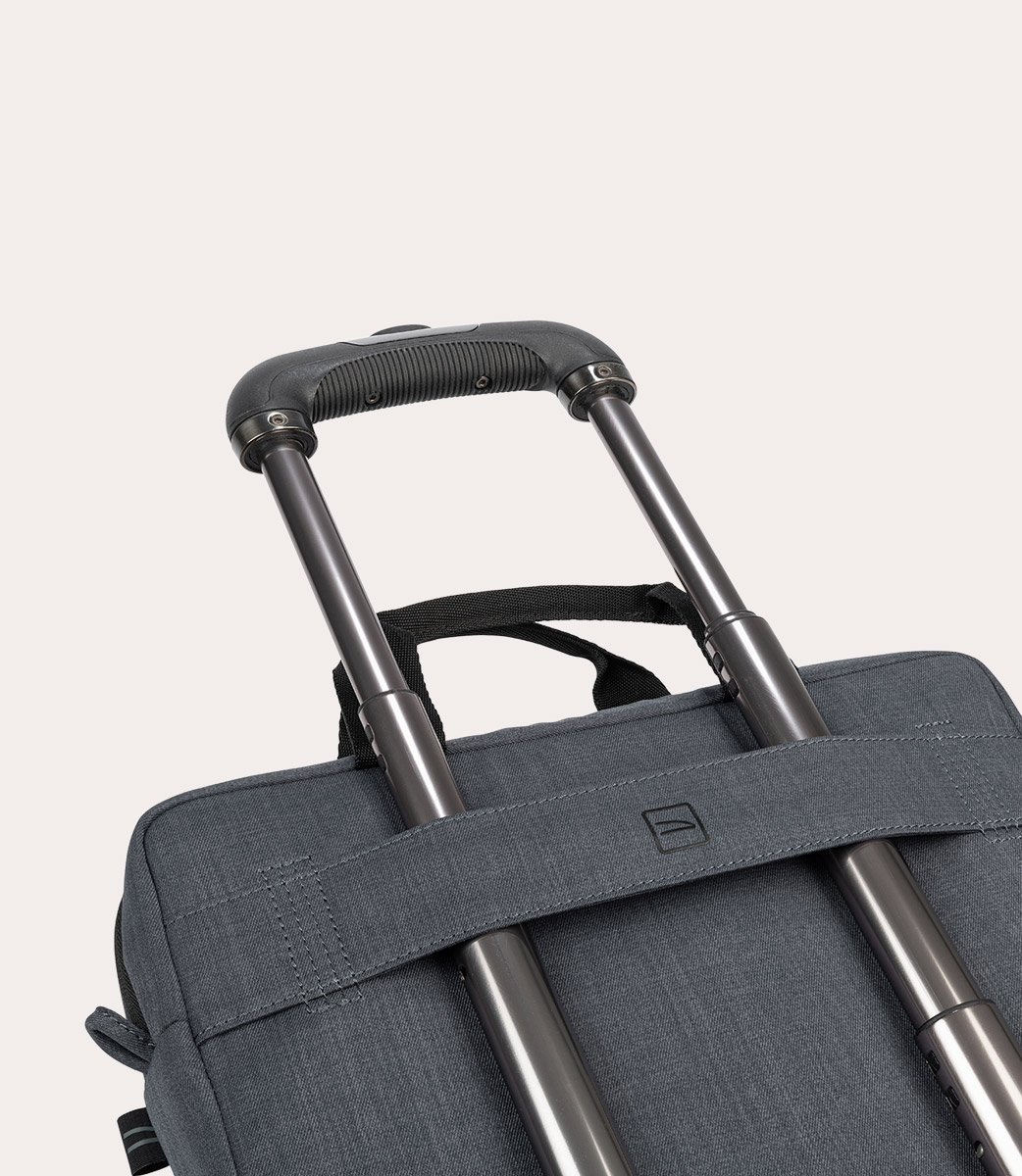 Primo piano di una valigia grigia con ruote. Il manico è nero e il telaio argentato. La borsa è grigia con un piccolo logo.