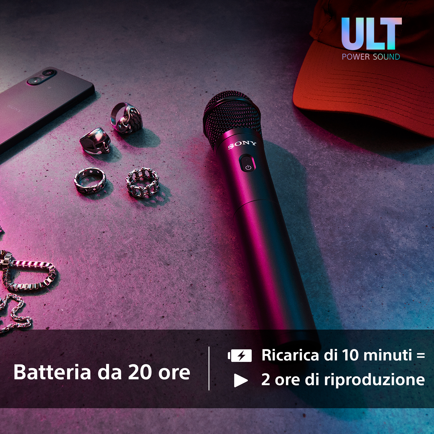 Mikrofon, pierścienie i telefon leżą na powierzchni. Czerwona czapka jest w tle. Tekst wskazuje na żywotność baterii i szybkie ładowanie.