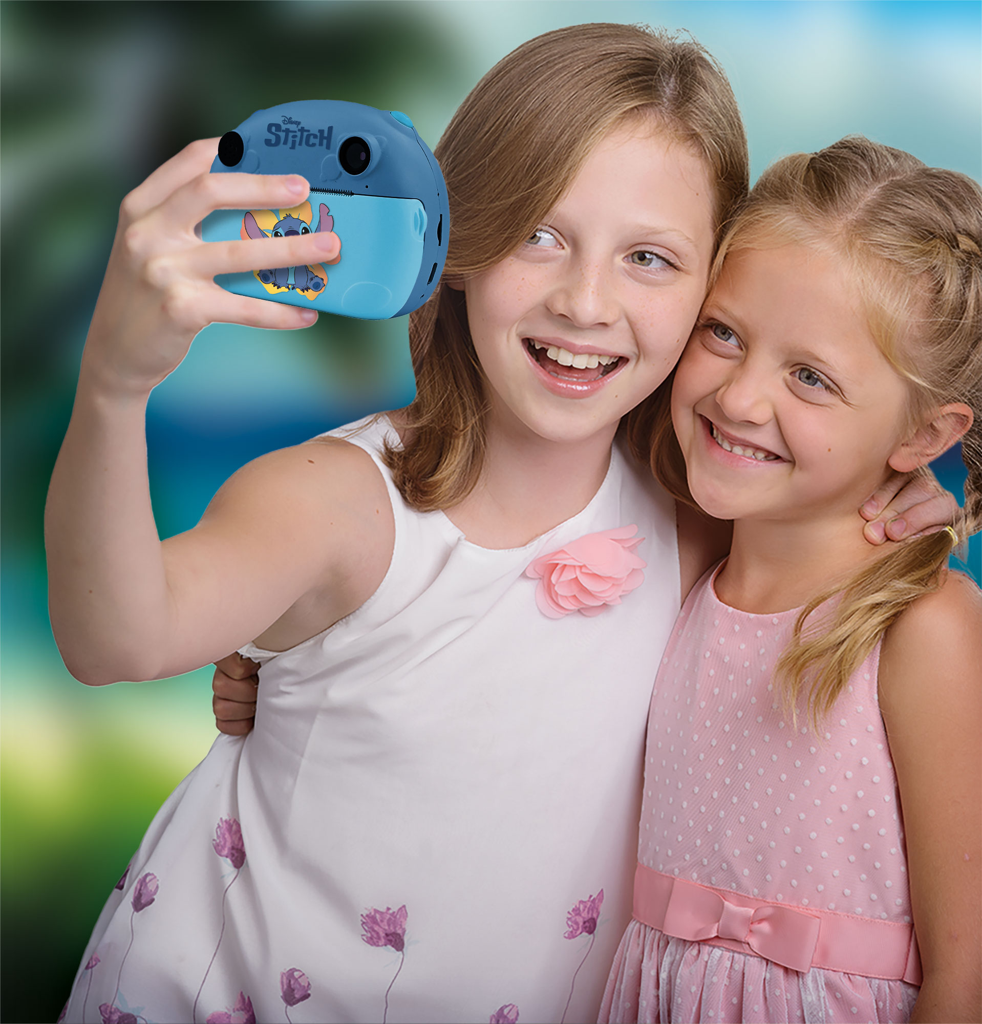 Zwei lächelnde Mädchen machen ein Selfie mit einer Stitch-Kamera. Ein Mädchen umarmt das andere, beide tragen Kleider.