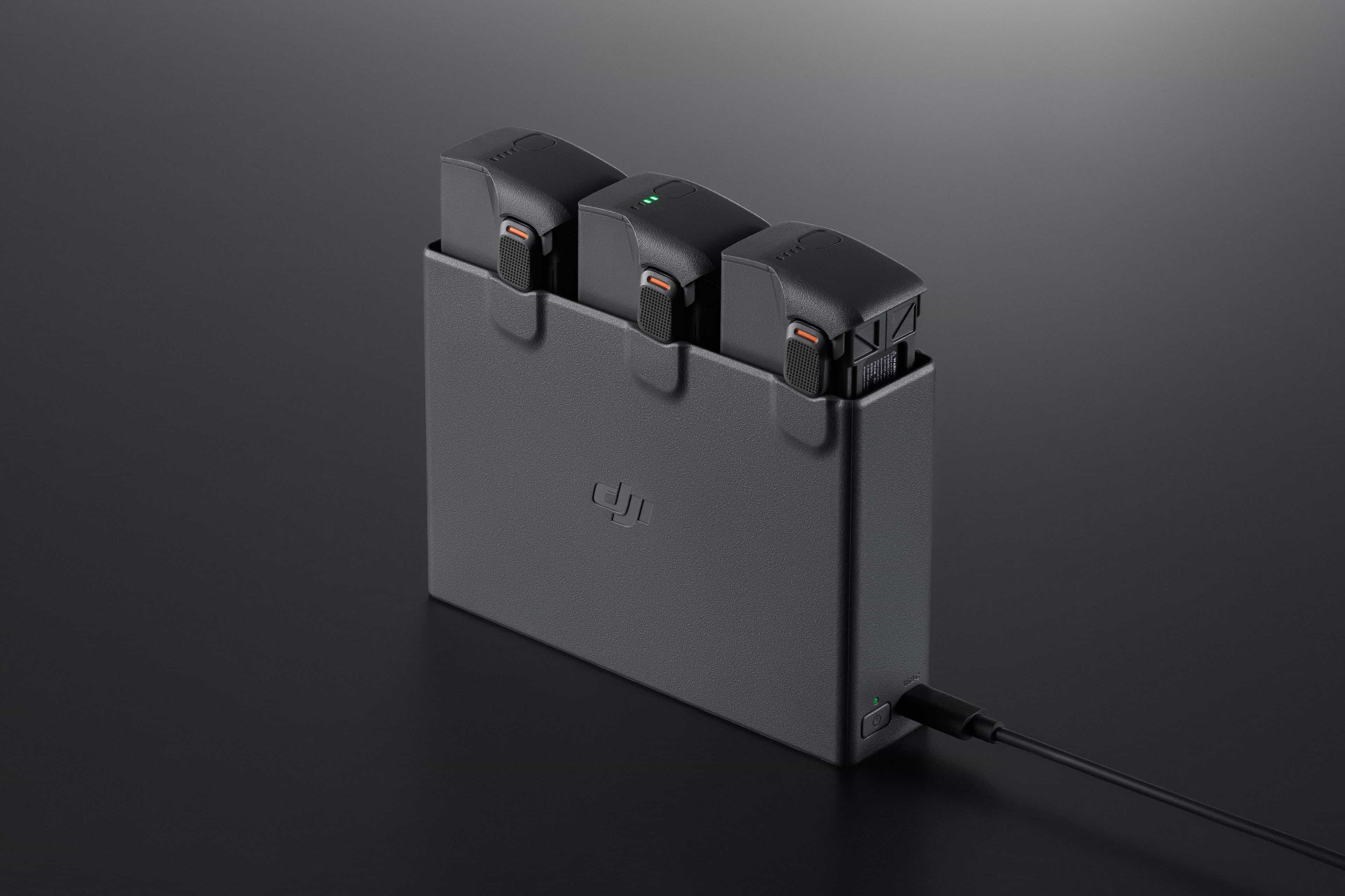 Un caricabatterie nero con tre batterie. Un cavo di ricarica è collegato. Lo sfondo è una superficie scura.