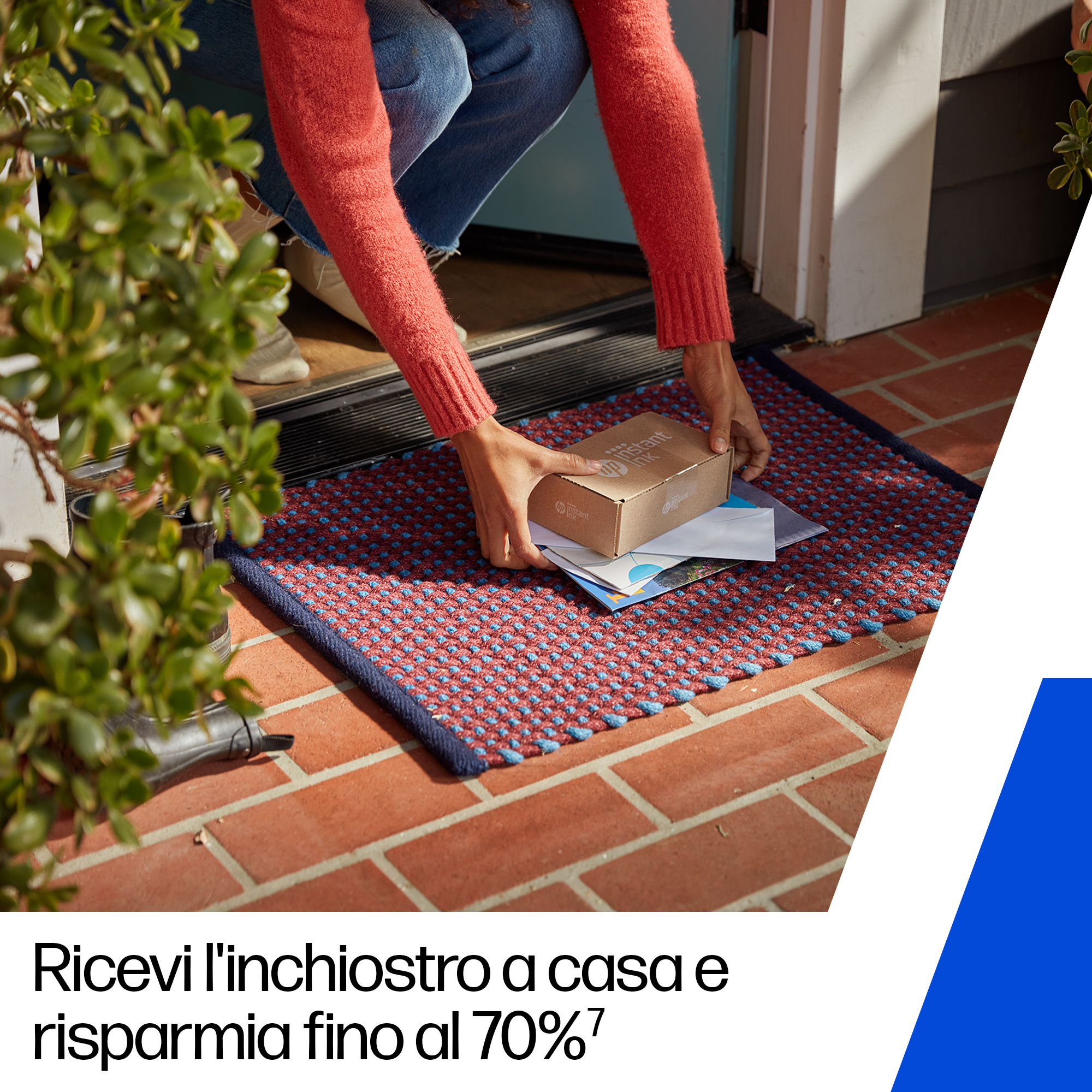 Una persona posiziona una scatola di cartone e della posta su uno zerbino. Lo zerbino è rosso e blu. La persona indossa jeans e un maglione rosso.
