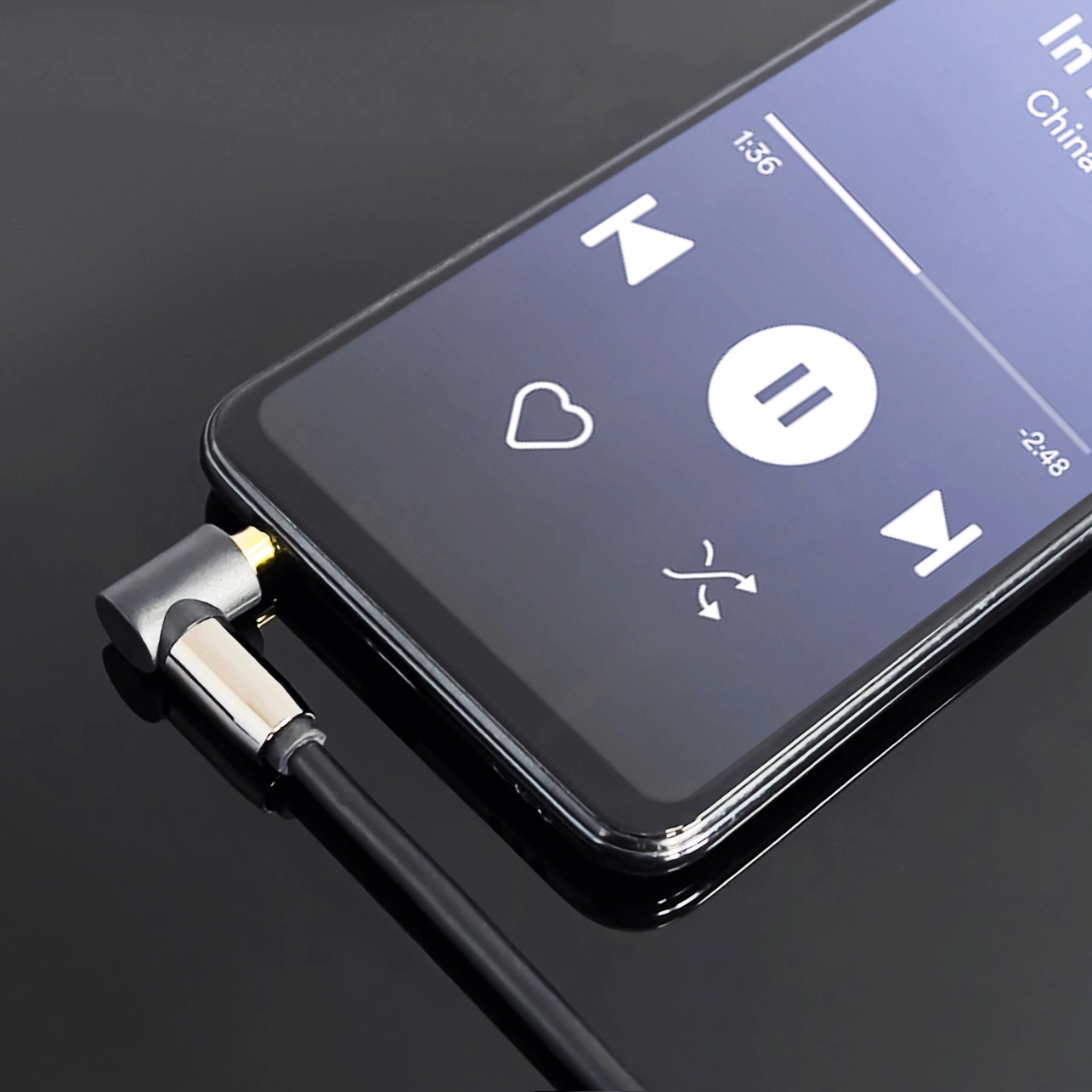 Ein Smartphone spielt Musik mit angeschlossenem Kopfhöreranschluss ab. Der Bildschirm zeigt Wiedergabesteuerungen. Das Telefon befindet sich auf einer reflektierenden Oberfläche.