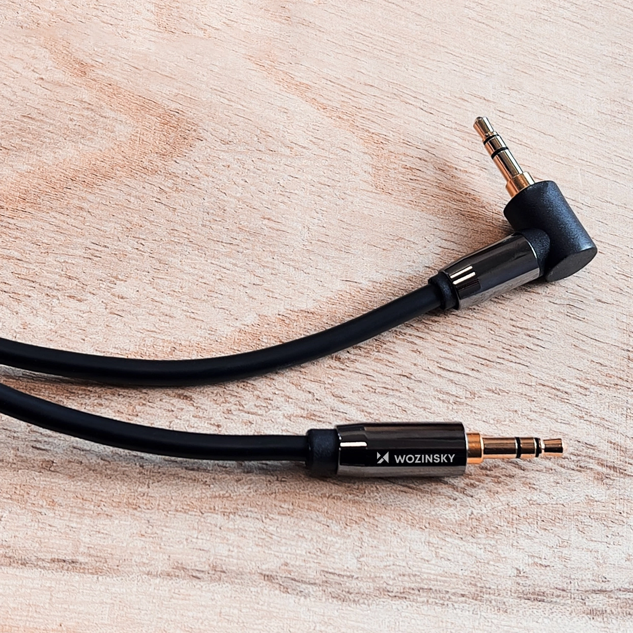 Ein schwarzes Audiokabel mit goldenen Steckern liegt auf einer Holzoberfläche. Ein Stecker ist abgewinkelt.