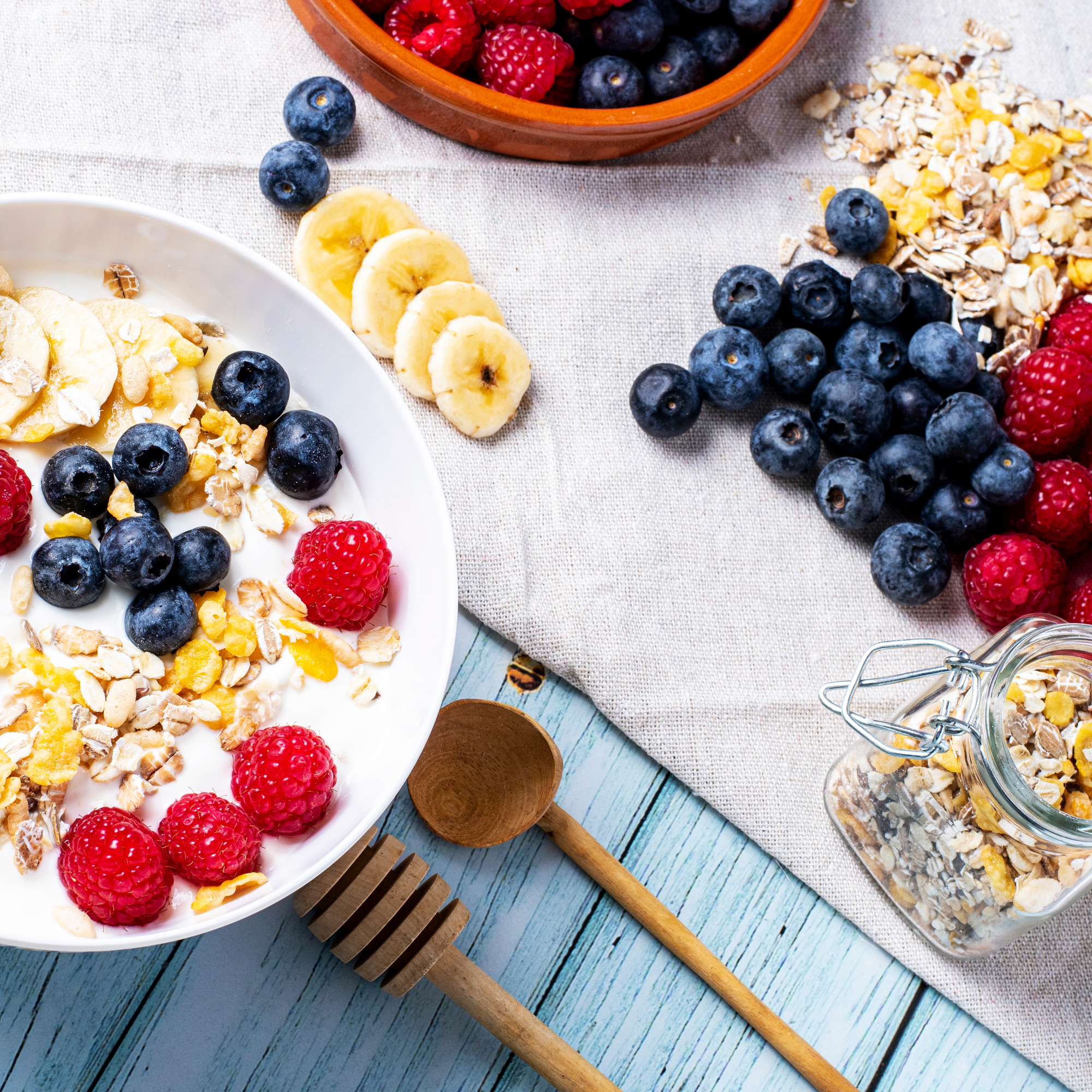 Vista dall'alto di yogurt con frutti di bosco e fettine di banana. Avena, frutti di bosco e miele su tavolo azzurro.