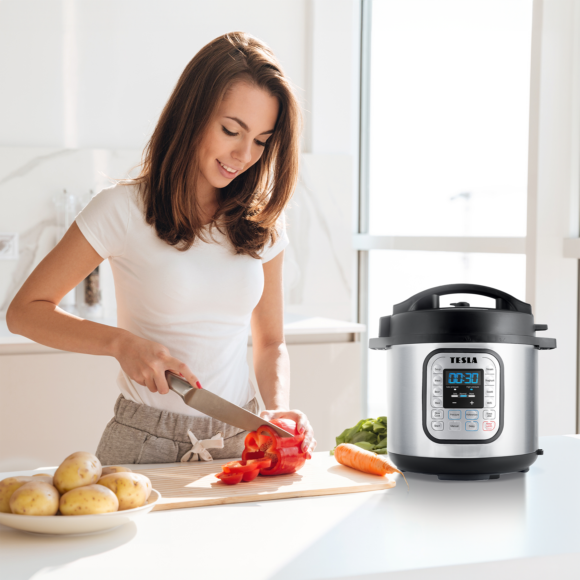 Una donna taglia un peperone rosso in cucina. Patate, una carota e una pentola a pressione sono anche sul tavolo.
