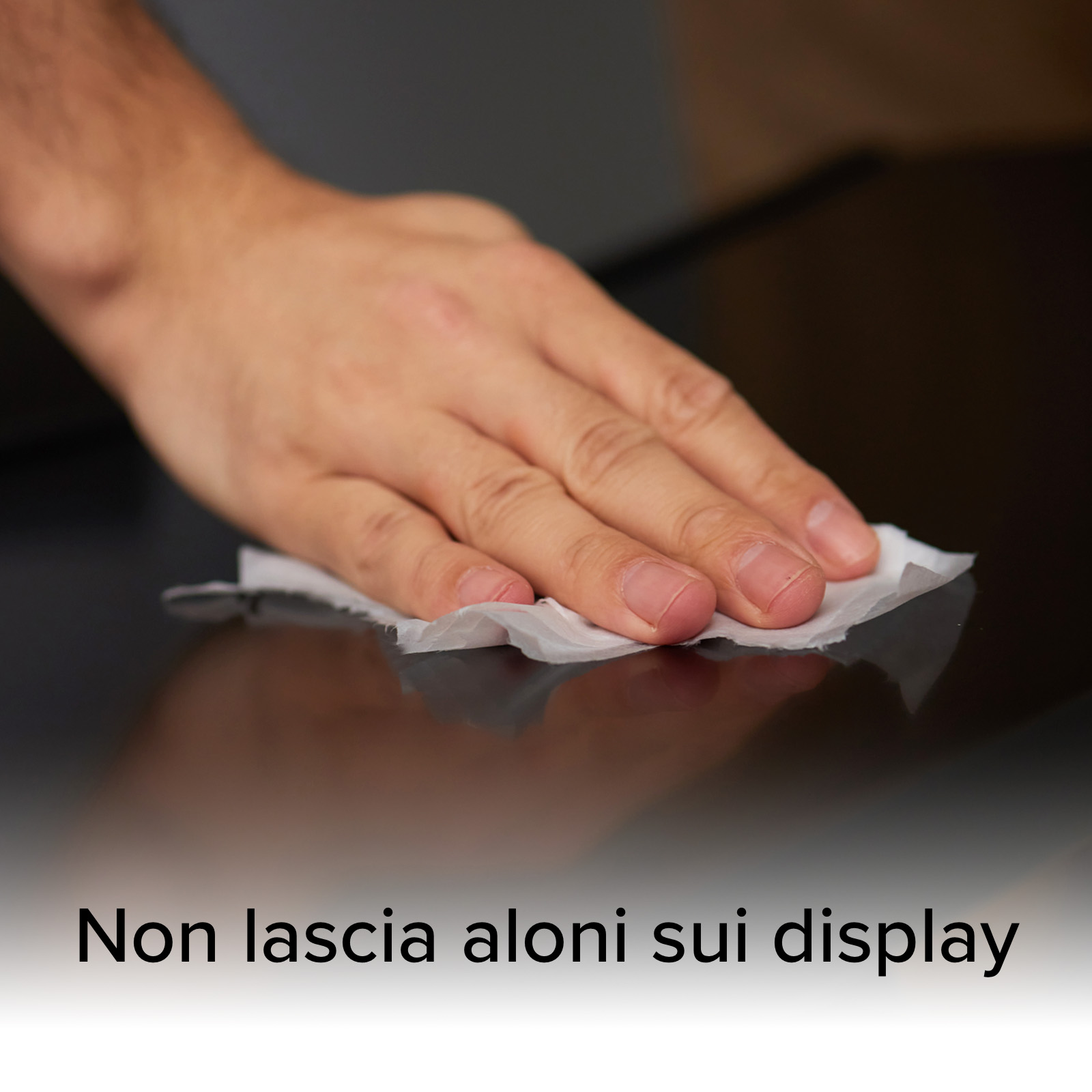 Una mano pulisce una superficie scura con una salvietta bianca. Il testo dice 'Non lascia aloni sui display'.