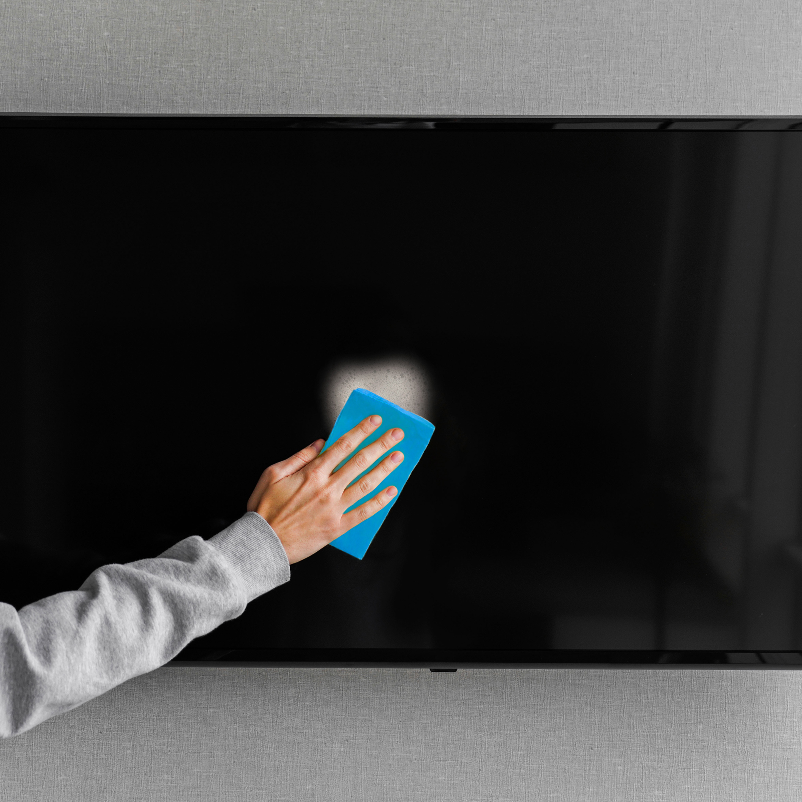 Una mano pulisce uno schermo TV nero con un panno blu. Una sezione è già pulita.