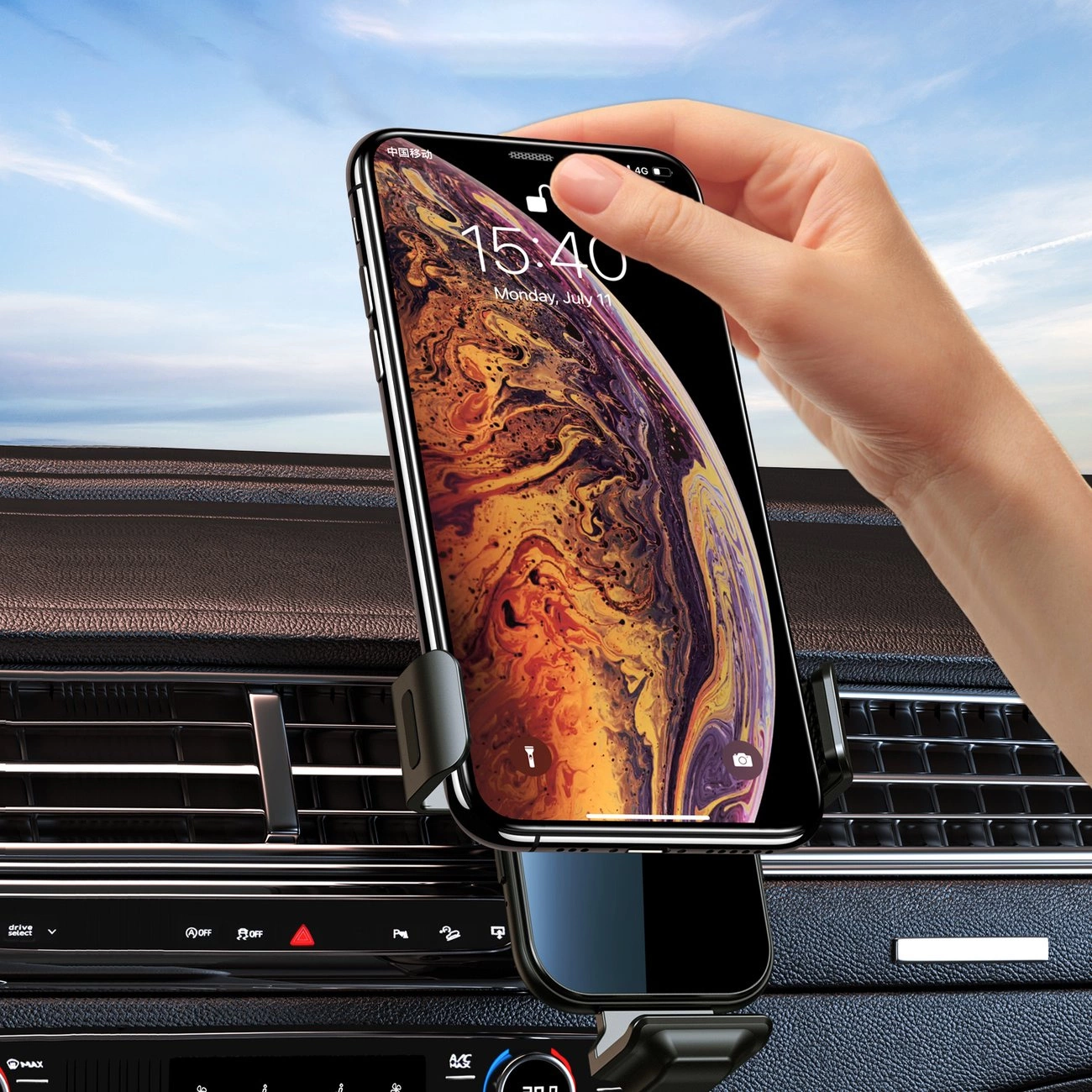 Eine Hand hält ein Smartphone in einer Autohalterung. Das Telefon zeigt eine Uhr, montiert auf einem Armaturenbrett, mit blauem Himmel.