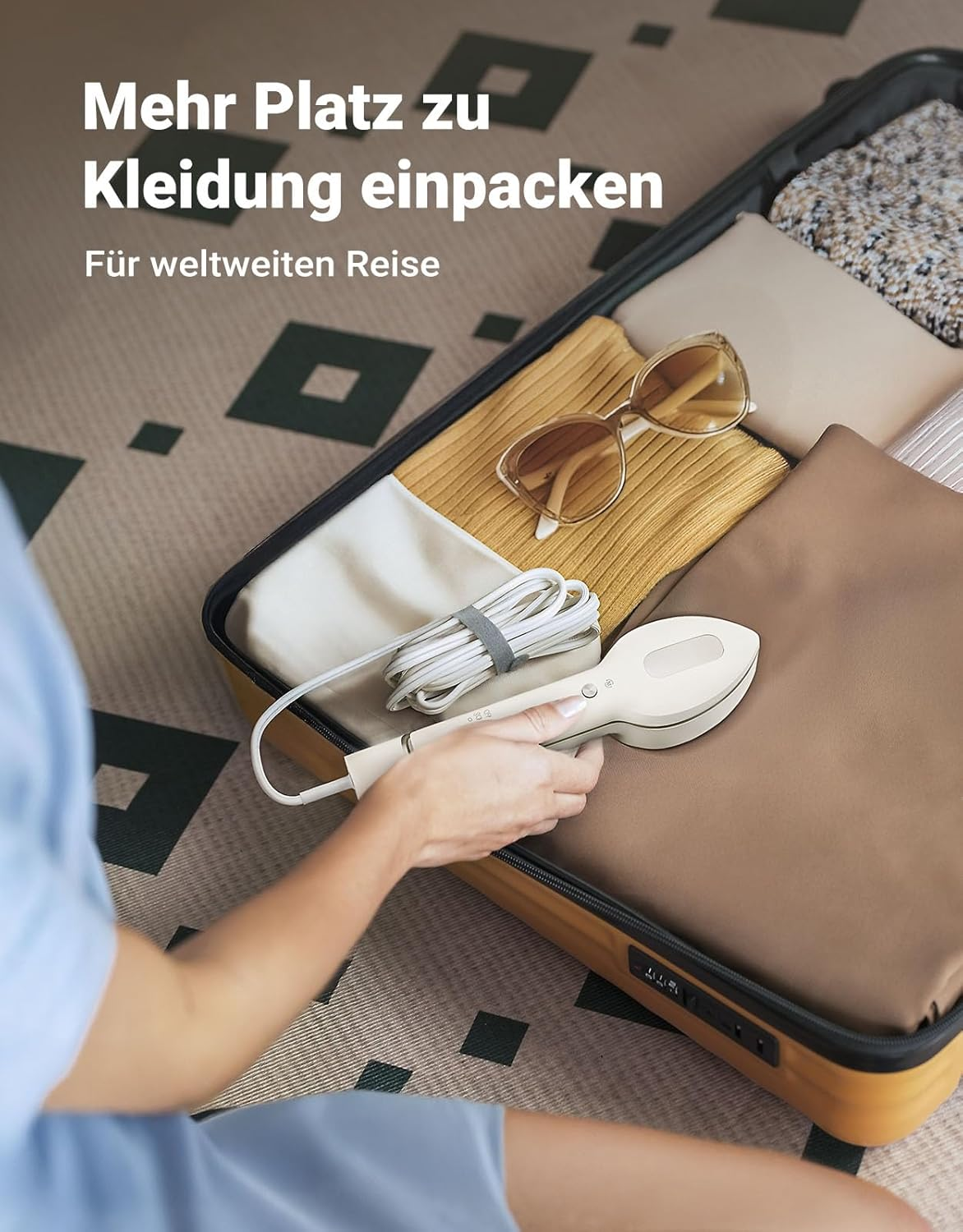 Eine Person verwendet einen Steamer auf Kleidung in einem offenen Koffer. Sonnenbrille und Kleidung sind im Koffer sichtbar.
