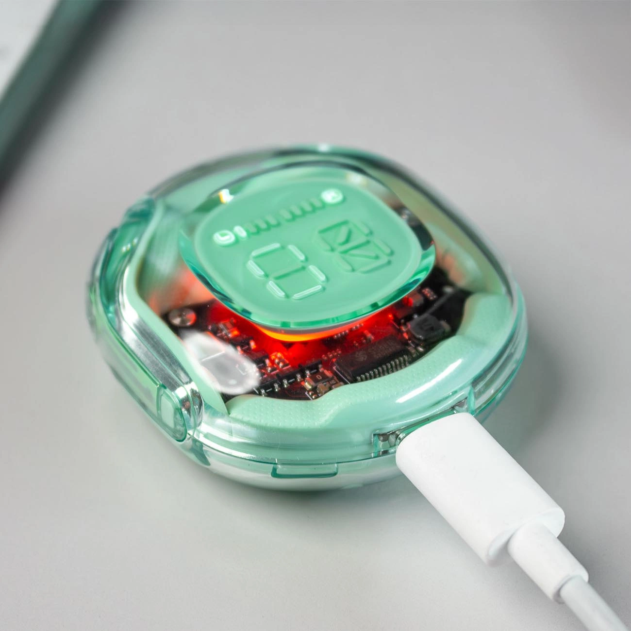 Un dispositivo elettronico verde menta con un display digitale che mostra '87'. Un cavo di ricarica bianco è collegato. Il dispositivo è su una superficie grigia.