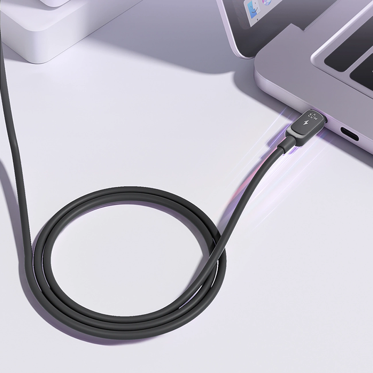 Un câble de chargement gris foncé est connecté à un ordinateur portable. Le câble forme une boucle sur une surface blanche.