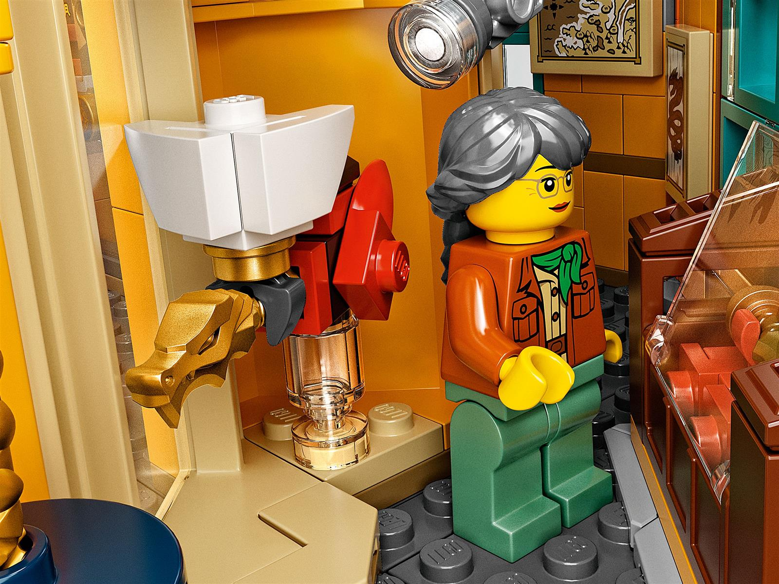 Eine Lego-Szene mit einer Frauenfigur, einer goldfarbenen drachenartigen Struktur und einer roten Maschine. Der Hintergrund ist eine detaillierte Inneneinrichtung.