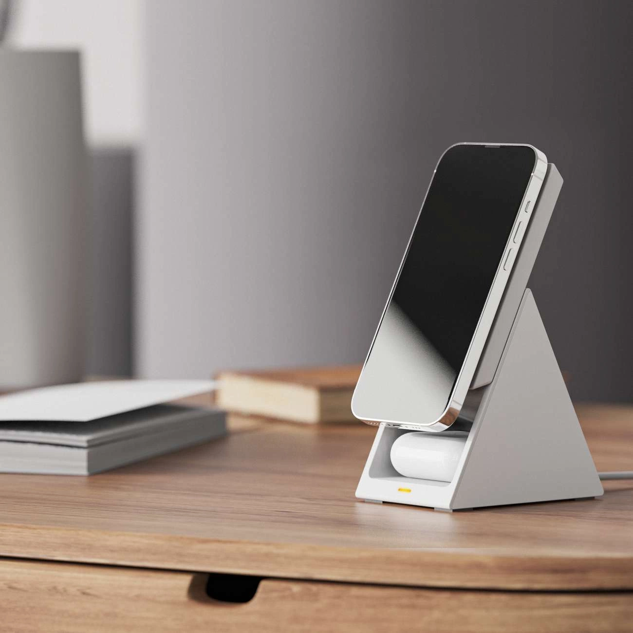 Ein weißes Telefonladegerät mit einem Telefon darauf, ein Paar Ohrhörer und ein Buch auf einem Holztisch.