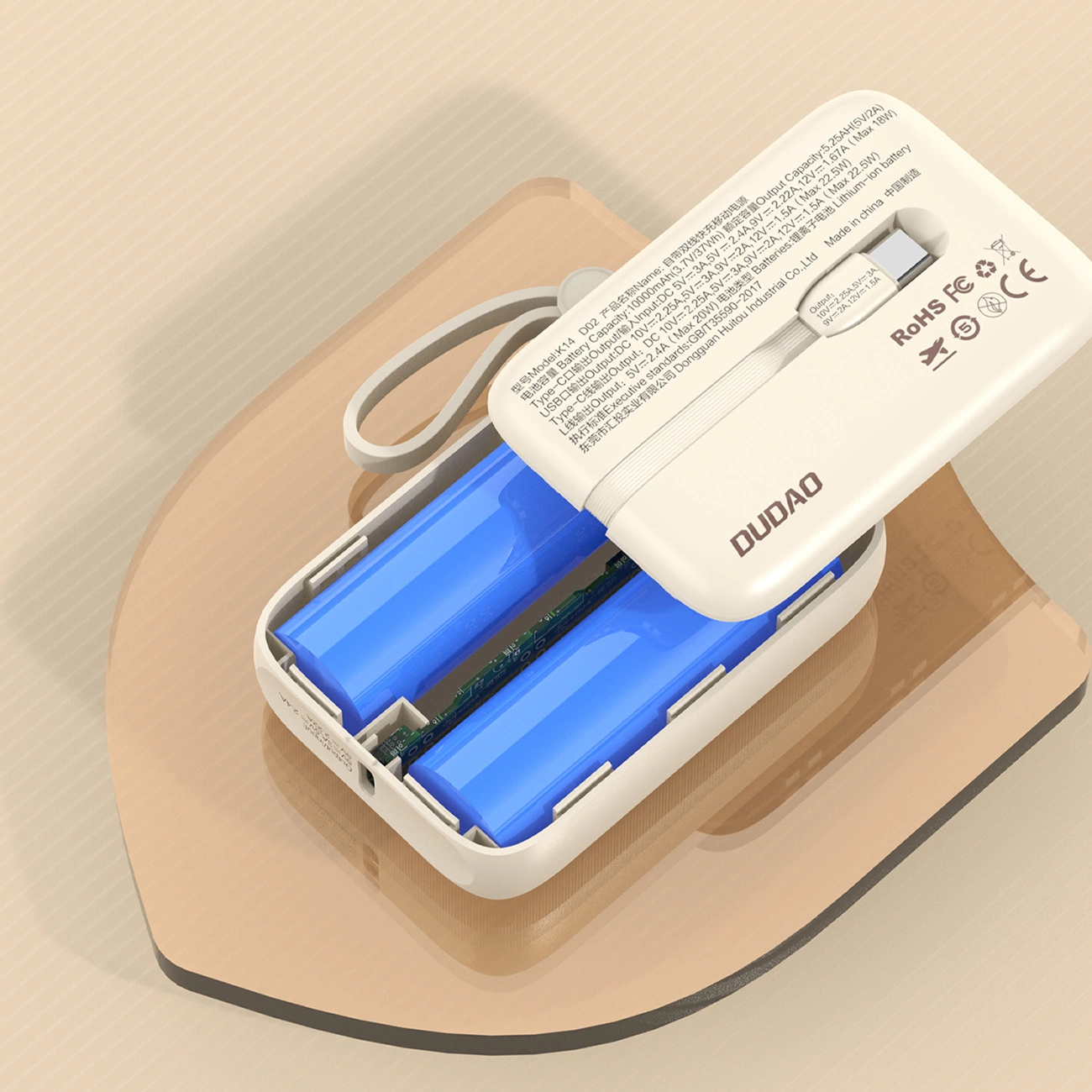 Power bank bianca con coperchio aperto, rivela due batterie blu. Su una superficie marrone arrotondata. Testo e loghi visibili.