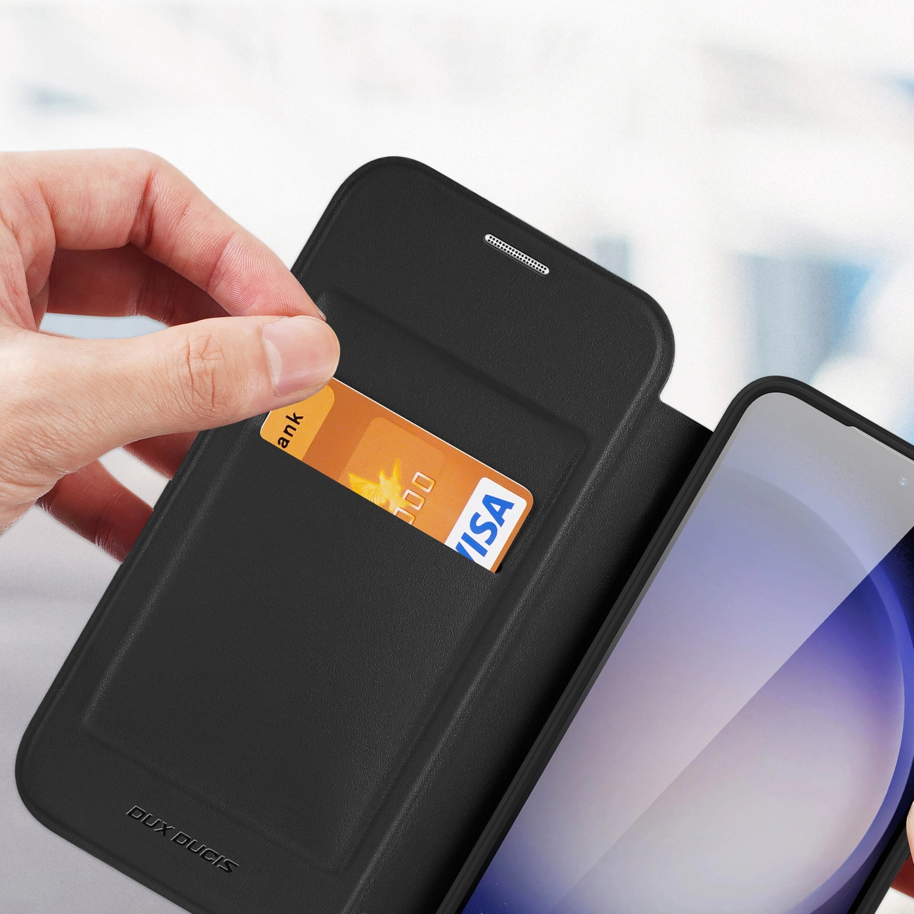 Una mano tiene una custodia per telefono con una carta di credito nella fessura. Il telefono è visibile a destra. La custodia è nera.