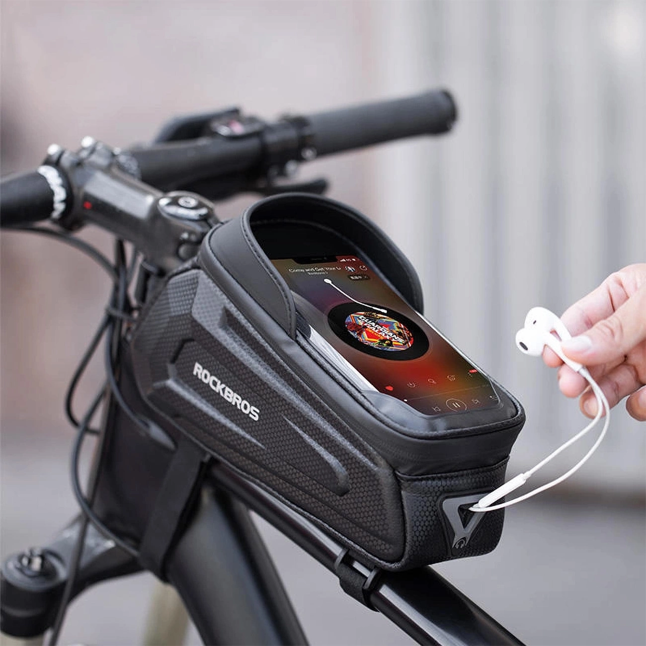 Una bici con una custodia per telefono sul manubrio, che mostra un telefono che riproduce musica. Una mano tiene auricolari bianchi.