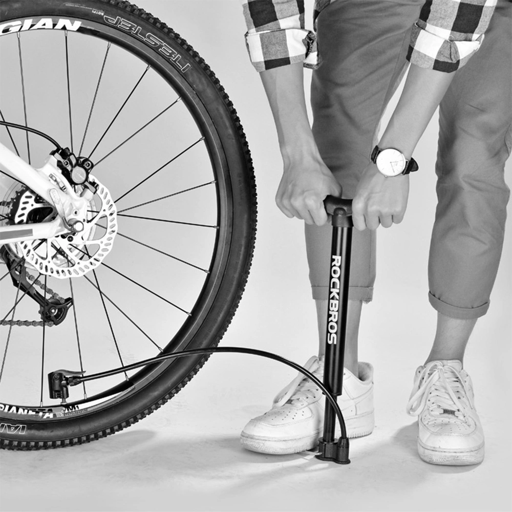 Una persona pompa la gomma di una bicicletta con una pompa Rockbros. La ruota della bici è visibile. La persona indossa un orologio e scarpe da ginnastica bianche.