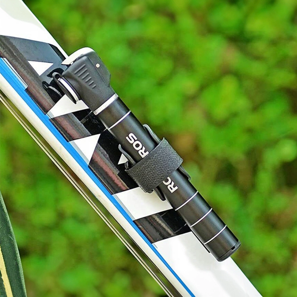 Eine schwarze Fahrradpumpe ist an einem Fahrradrahmen befestigt. Sie wird von einem schwarzen Riemen gehalten. Grünes Laub ist im Hintergrund.