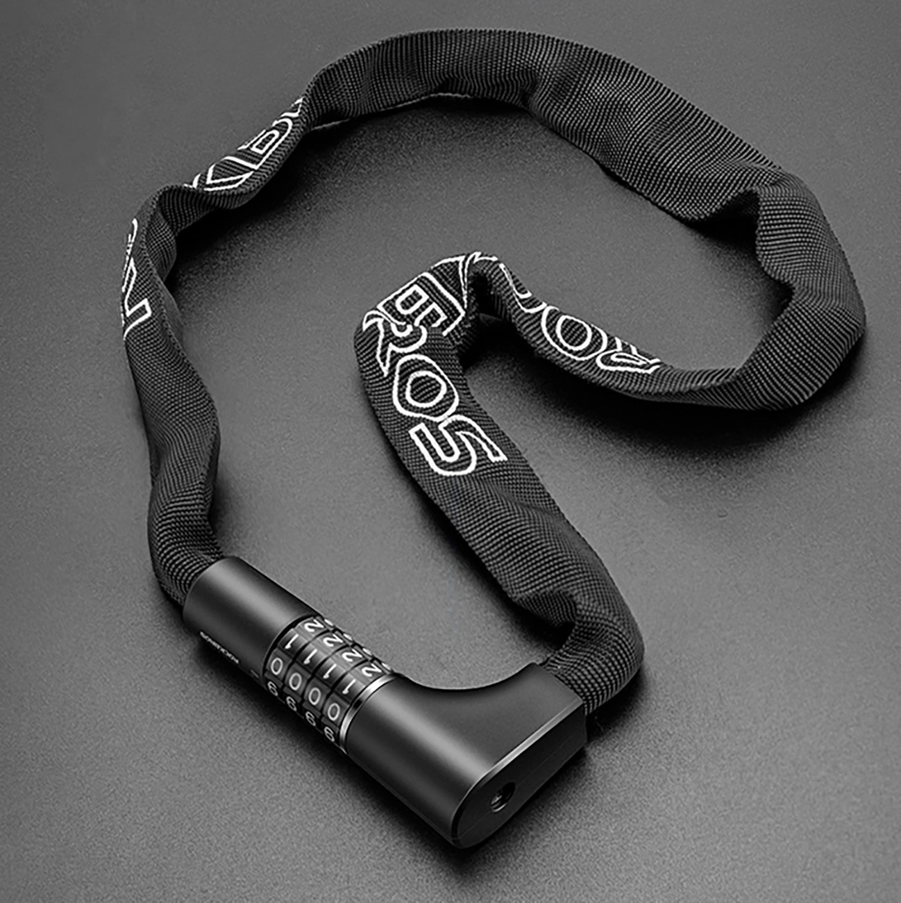 Lucchetto per catena da bici nero con testo bianco, serratura a combinazione, su superficie grigio scuro. Il lucchetto è ad anello.