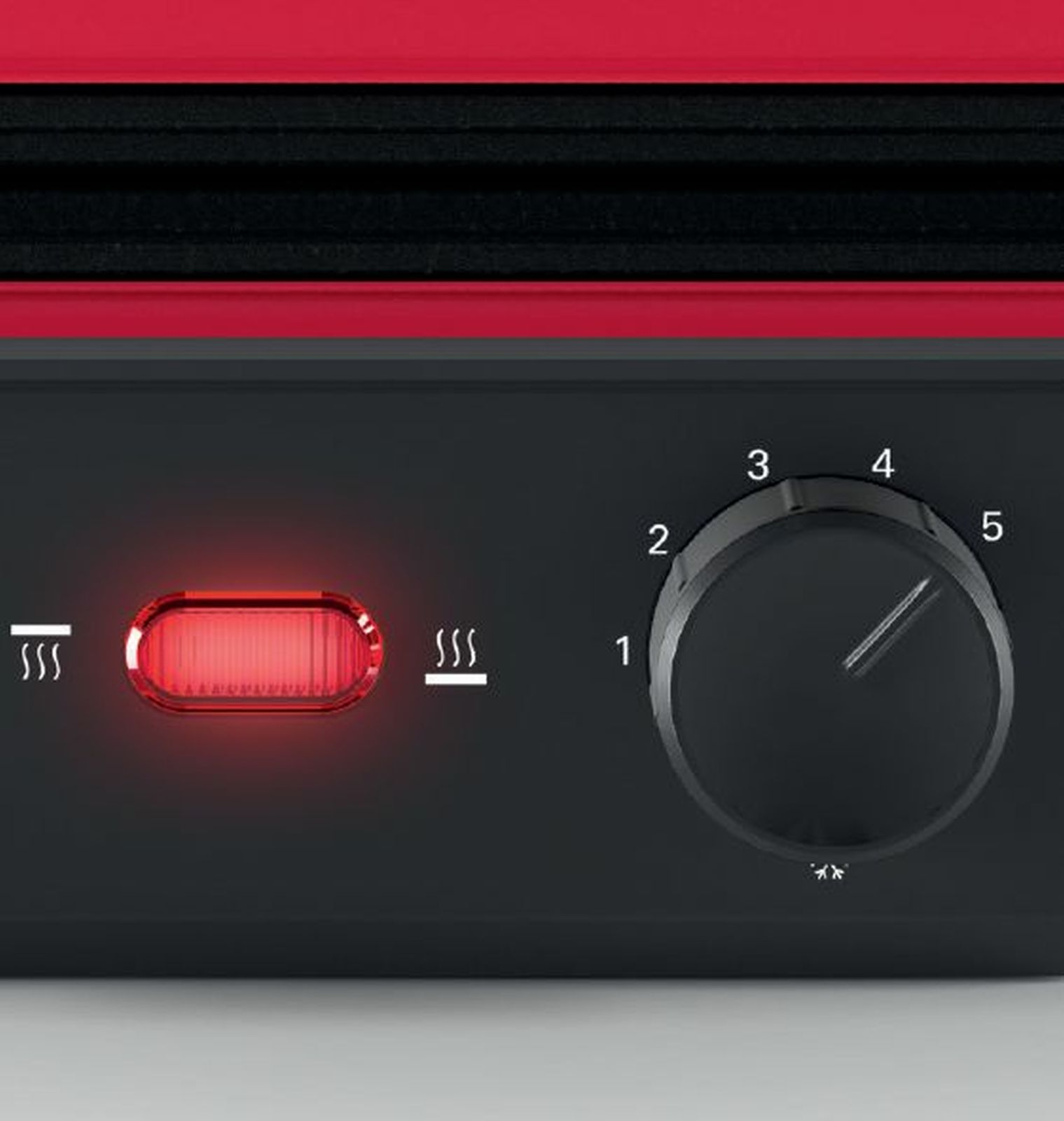 Primer plano de un electrodoméstico negro y rojo. Tiene un dial con los números 1-5, una luz roja y símbolos de calor.